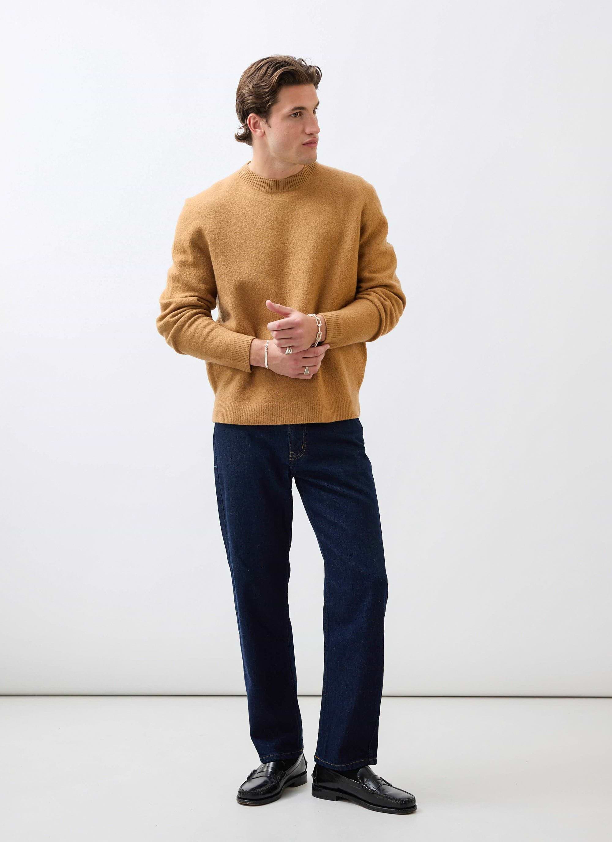A model wears the brown Felted Wool Jumper from Percival with dark blue jeans and black loafers in a studio.
