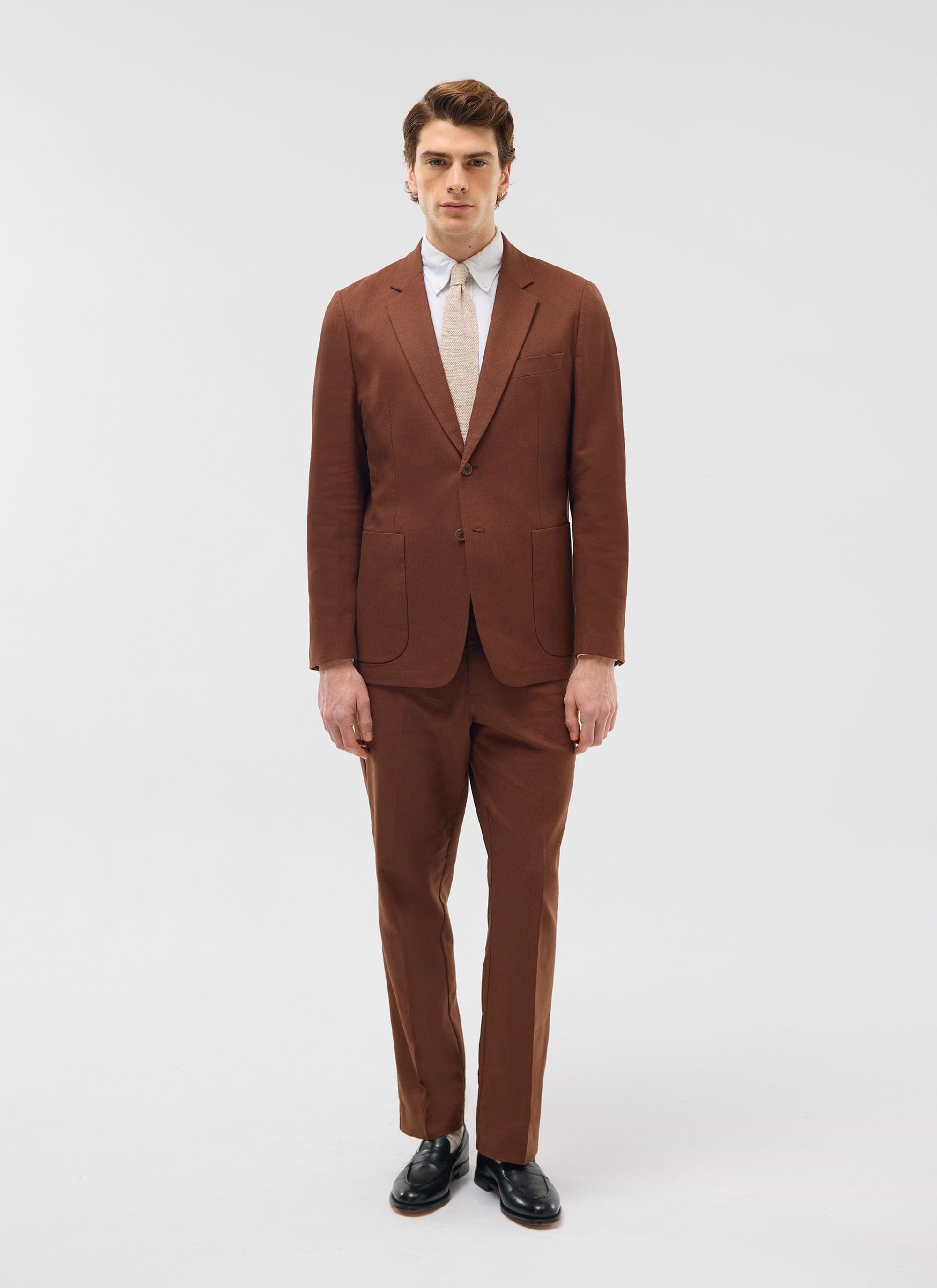 A model wears the Percival Tailored Linen Trousers in brown, styled with the matching blazer against a white background.