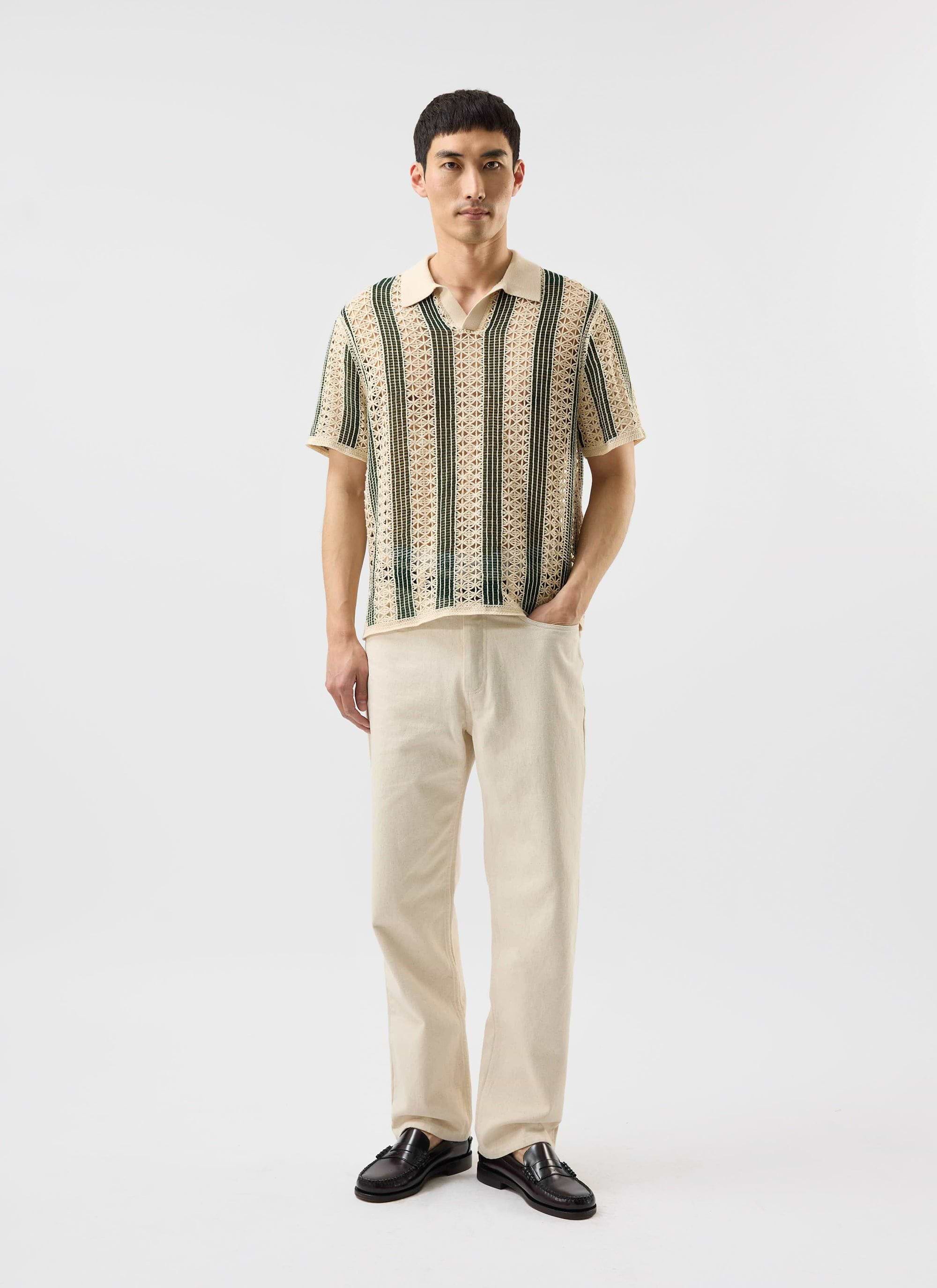 A man models the Percival Sarti Knitted Polo Shirt in ecru with forest green stripes, paired with cream trousers.