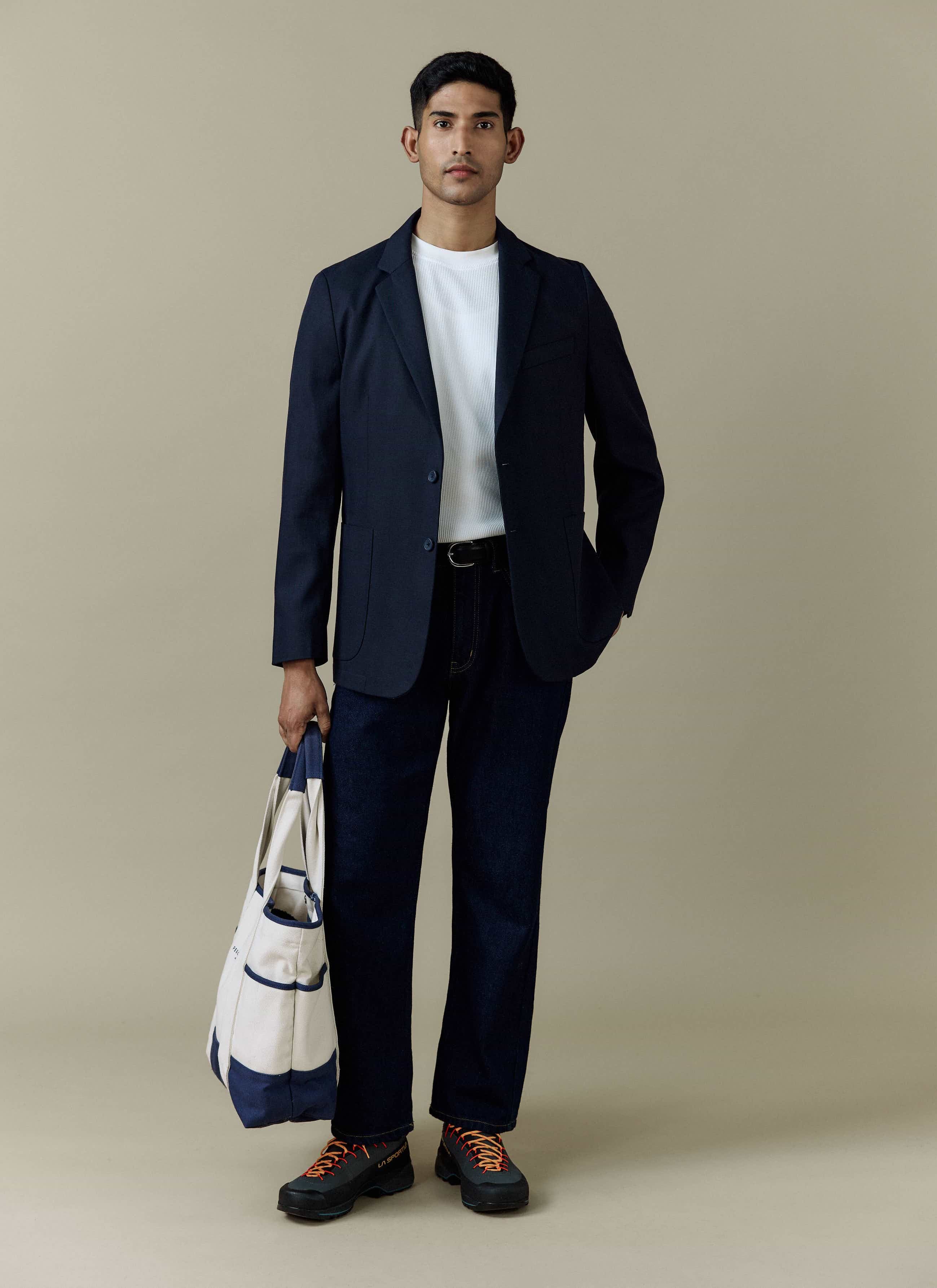 A model wears the navy Lyocell Regular Blazer by Percival, styled with a white tee, dark jeans, and holding a tote bag.
