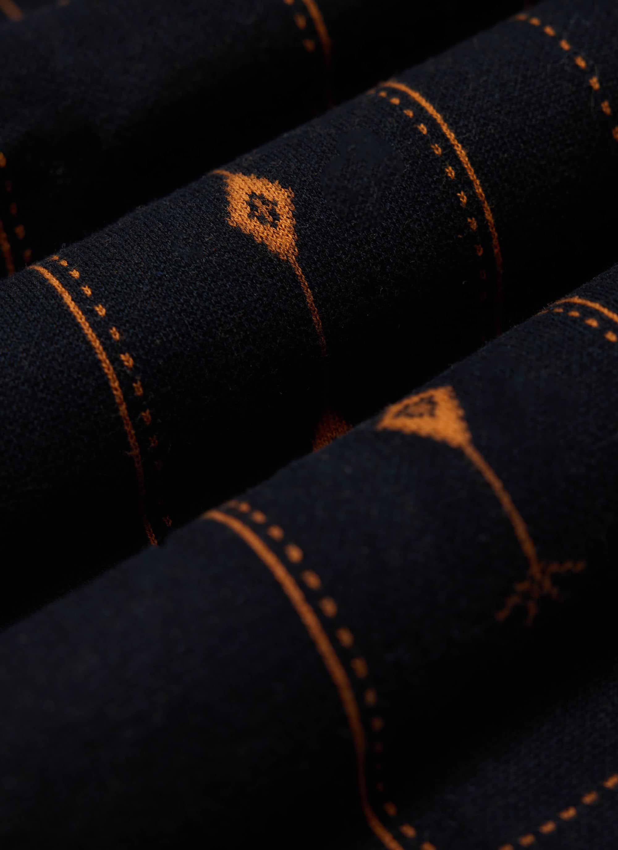 A close-up shot of the folded dark navy Percival Folio Knitted Shirt, detailing the tobacco book spine jacquard knit.