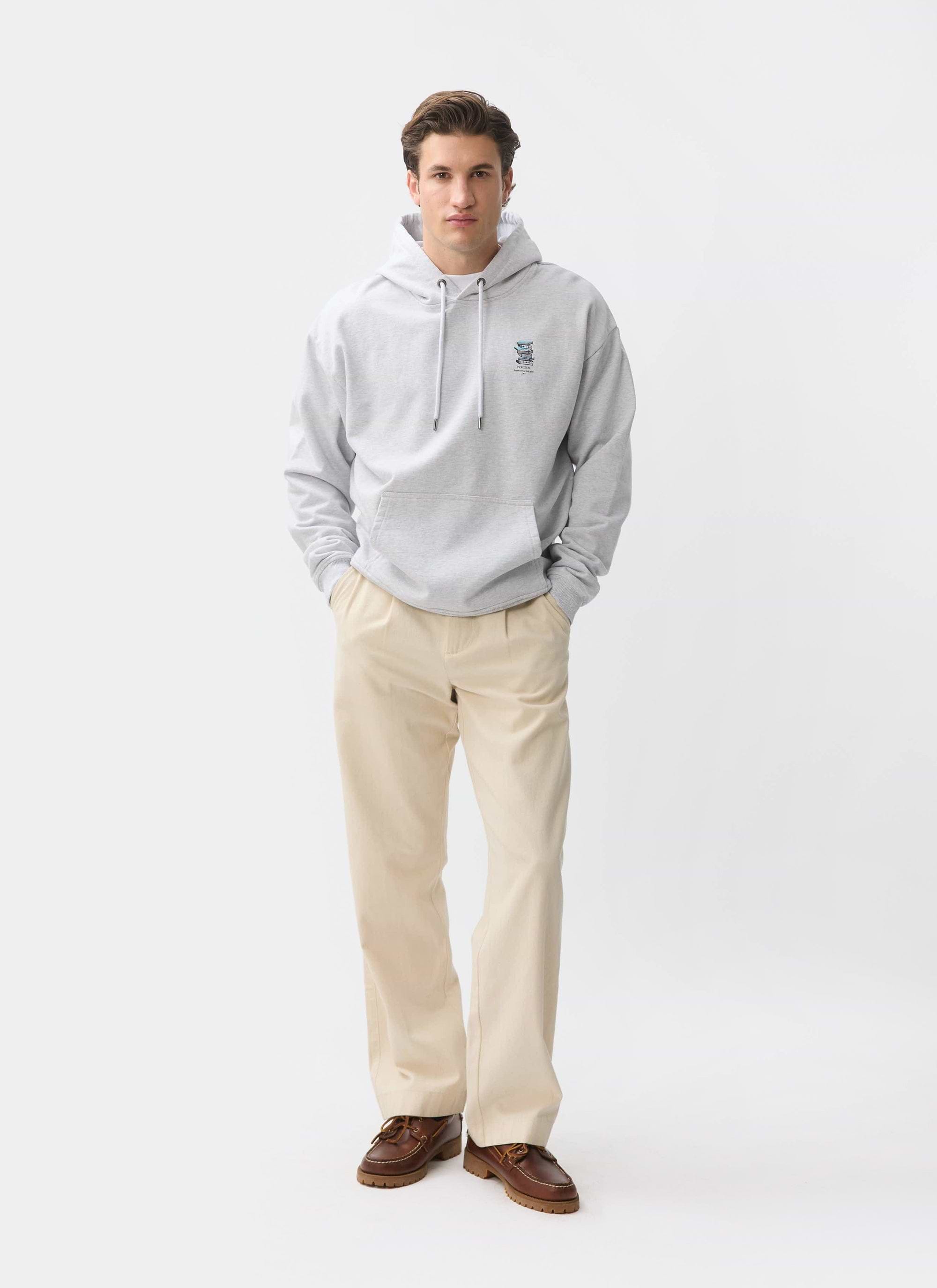 A model wears the Percival Duke Hoodie in grey, styled with cream trousers and brown shoes against a white studio background.