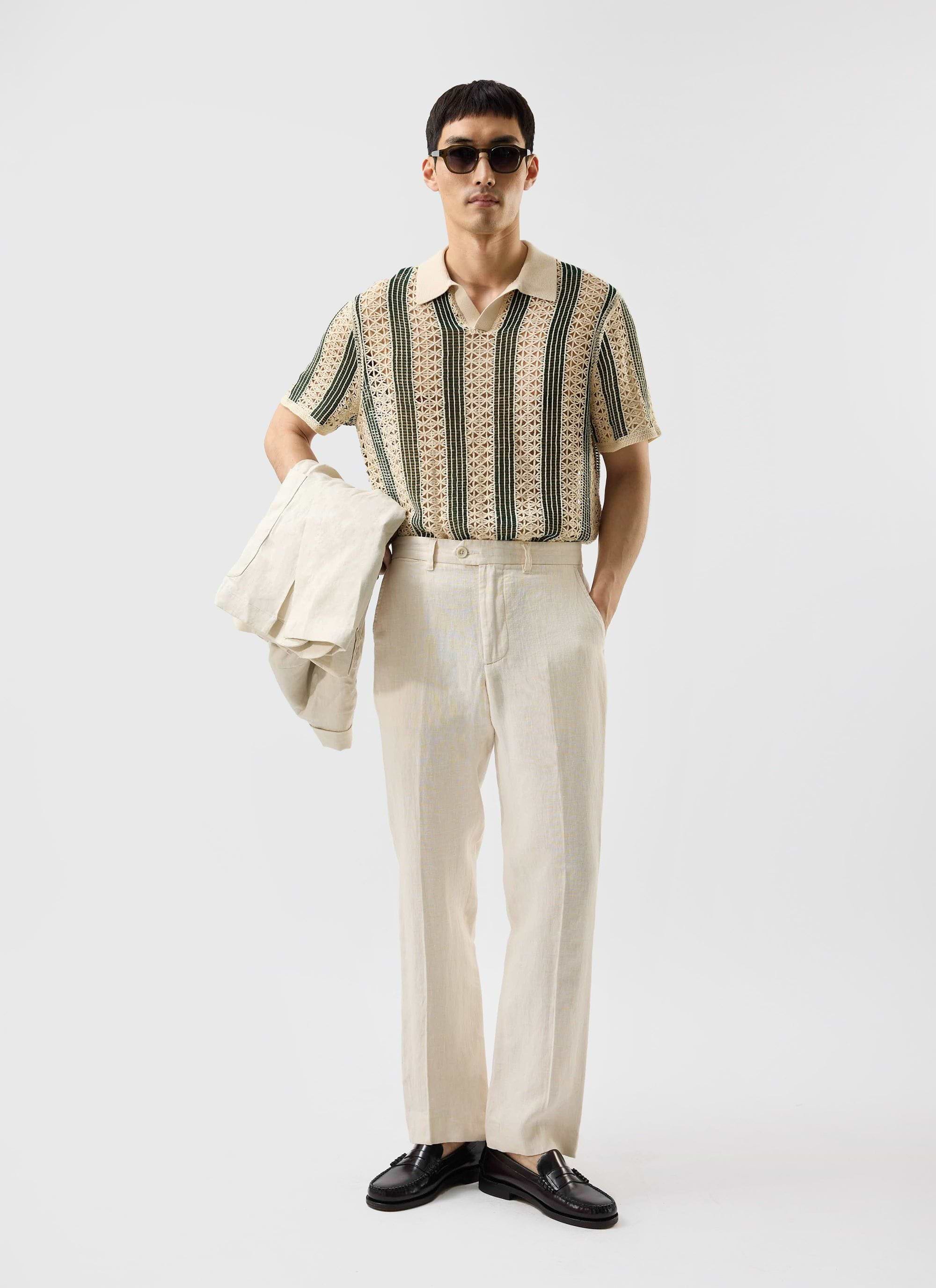 A model wears the Percival Sarti Knitted Polo in ecru and forest green, styled with cream trousers and sunglasses.