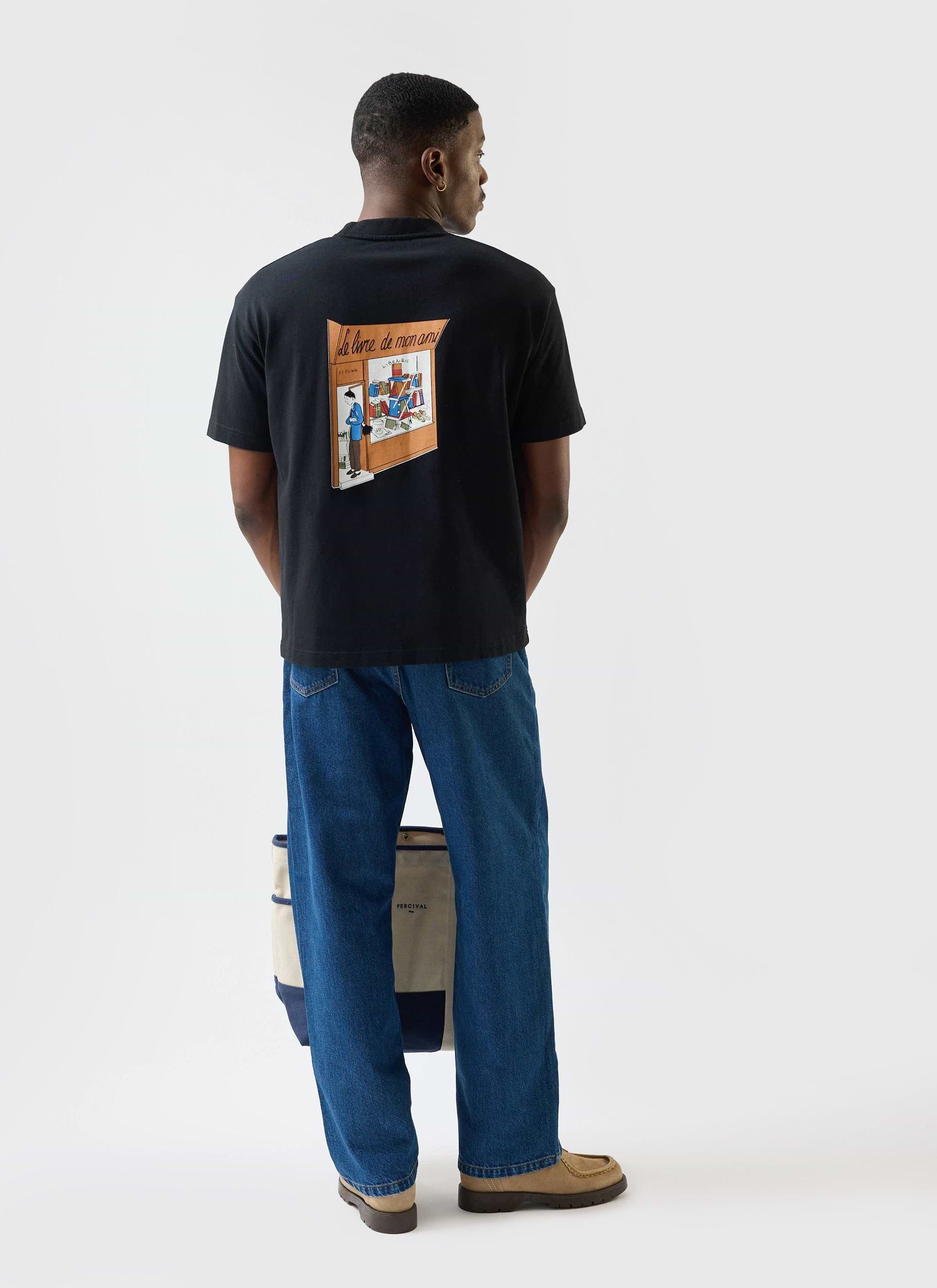 A model from behind wears the black Percival Le Livre De Mon Ami t-shirt, showing the colourful bookshop graphic on the back.