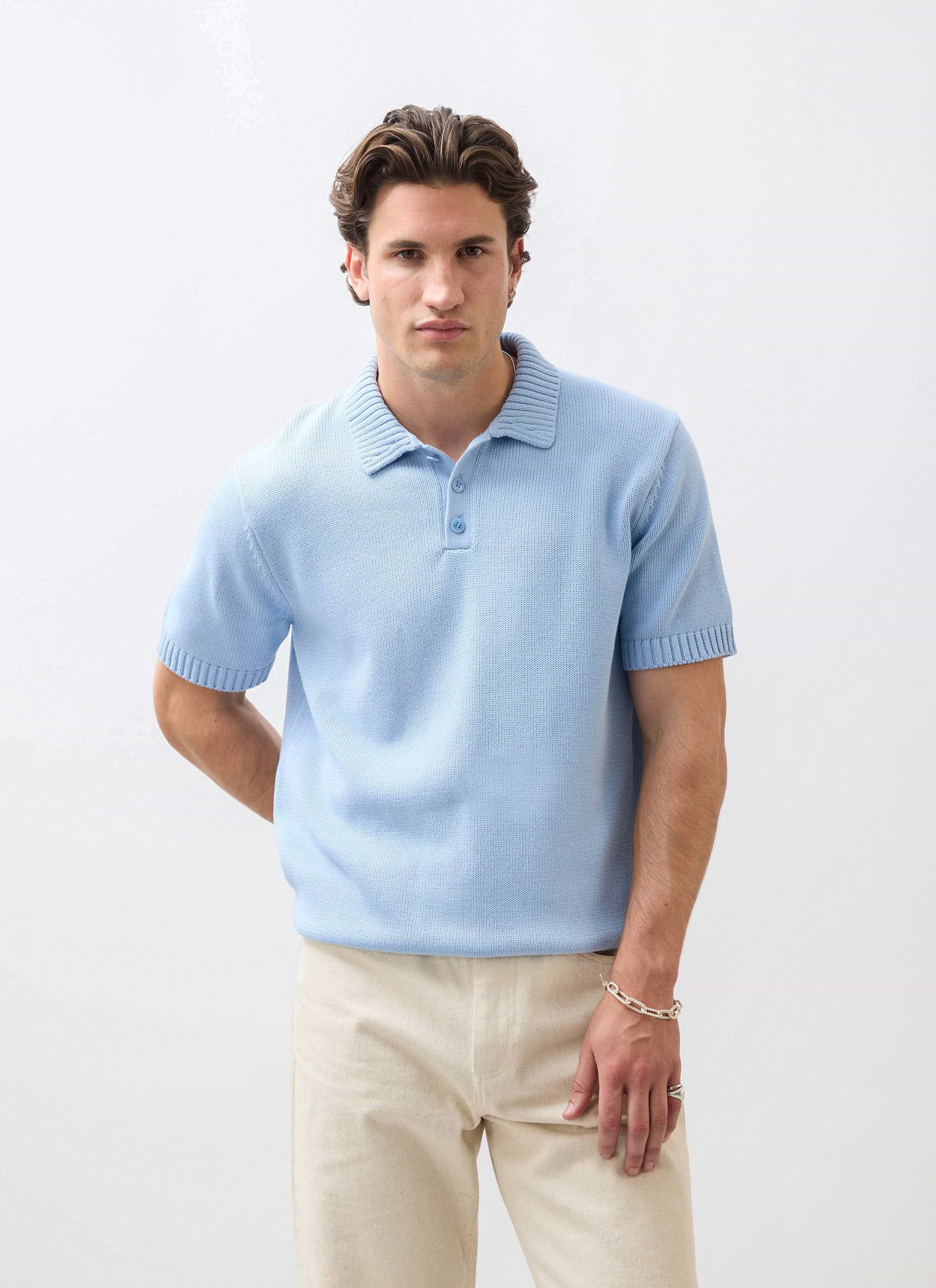 A man models the Percival Verso Short Sleeve Knitted Shirt in heather blue, styled with cream trousers.