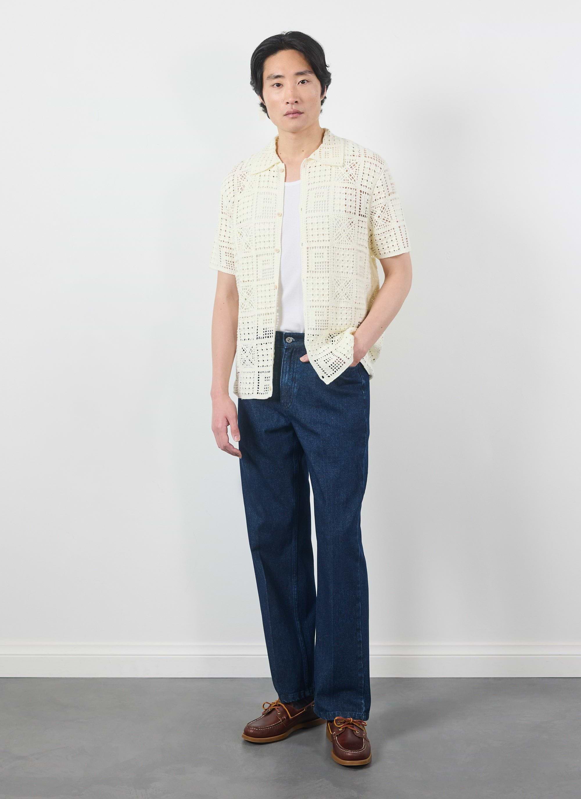 A model wears the Percival Crochet Groundsman Shirt in ecru, styled open over a t-shirt with dark jeans and boat shoes.