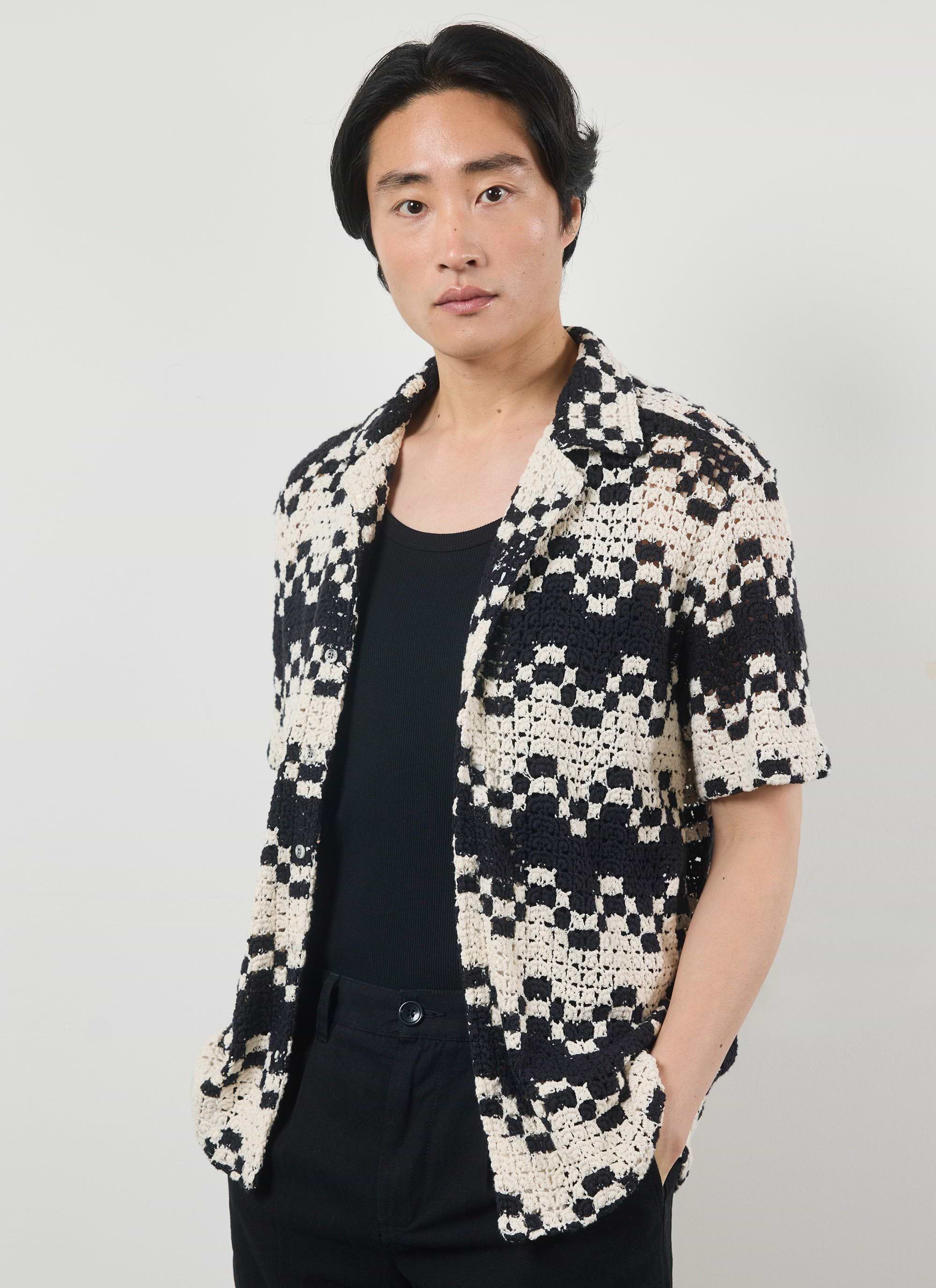 A model wears the Percival Naples Crochet Cuban Shirt in ecru and black, styled open over a black vest and trousers.