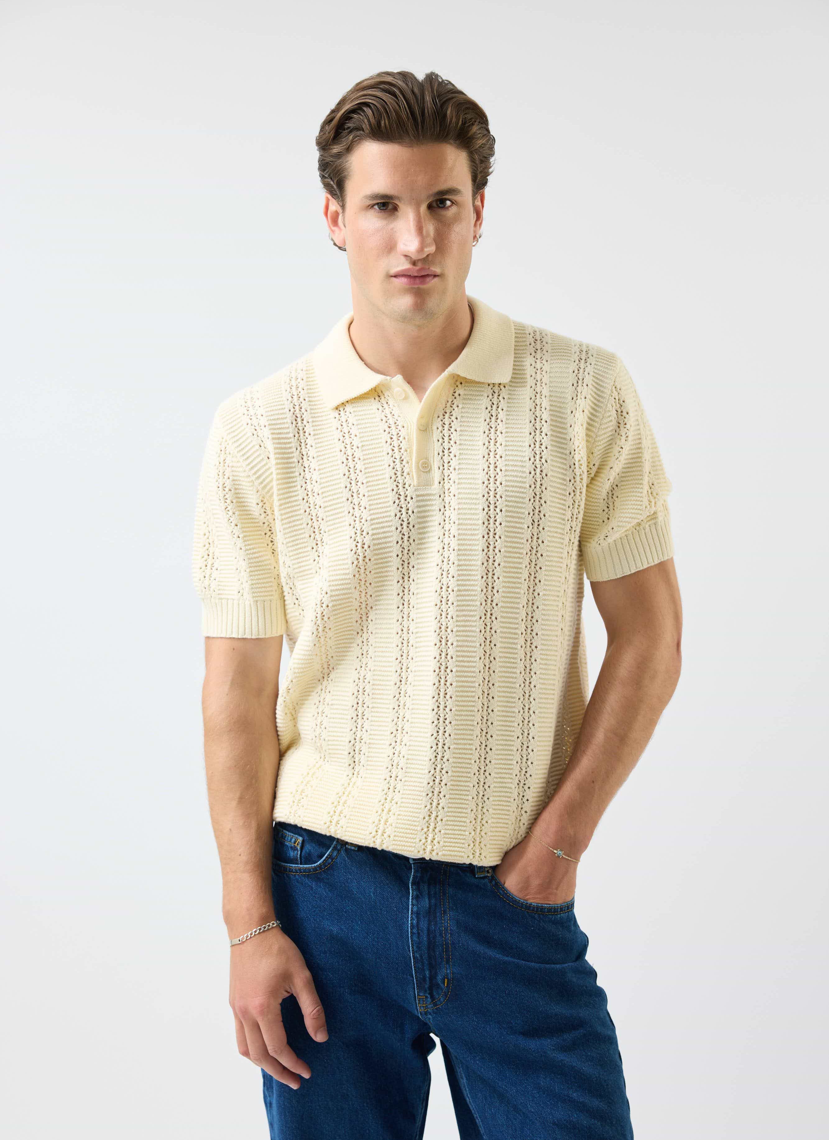 A model wears the Percival Addendum Knitted Polo Shirt in ecru cream, showing off its detailed tonal jacquard knit.