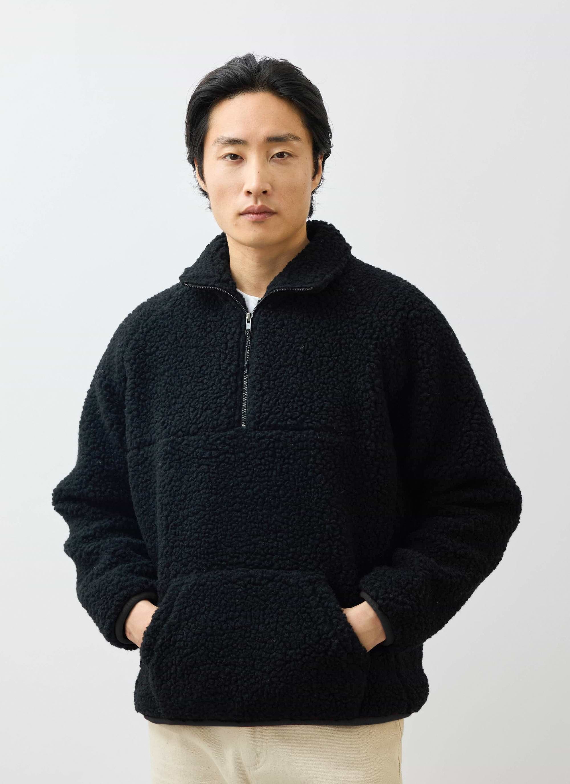 A model wears the Percival black Quarter Zip Wool Fleece Pullover, standing with his hands in the front kangaroo pocket.