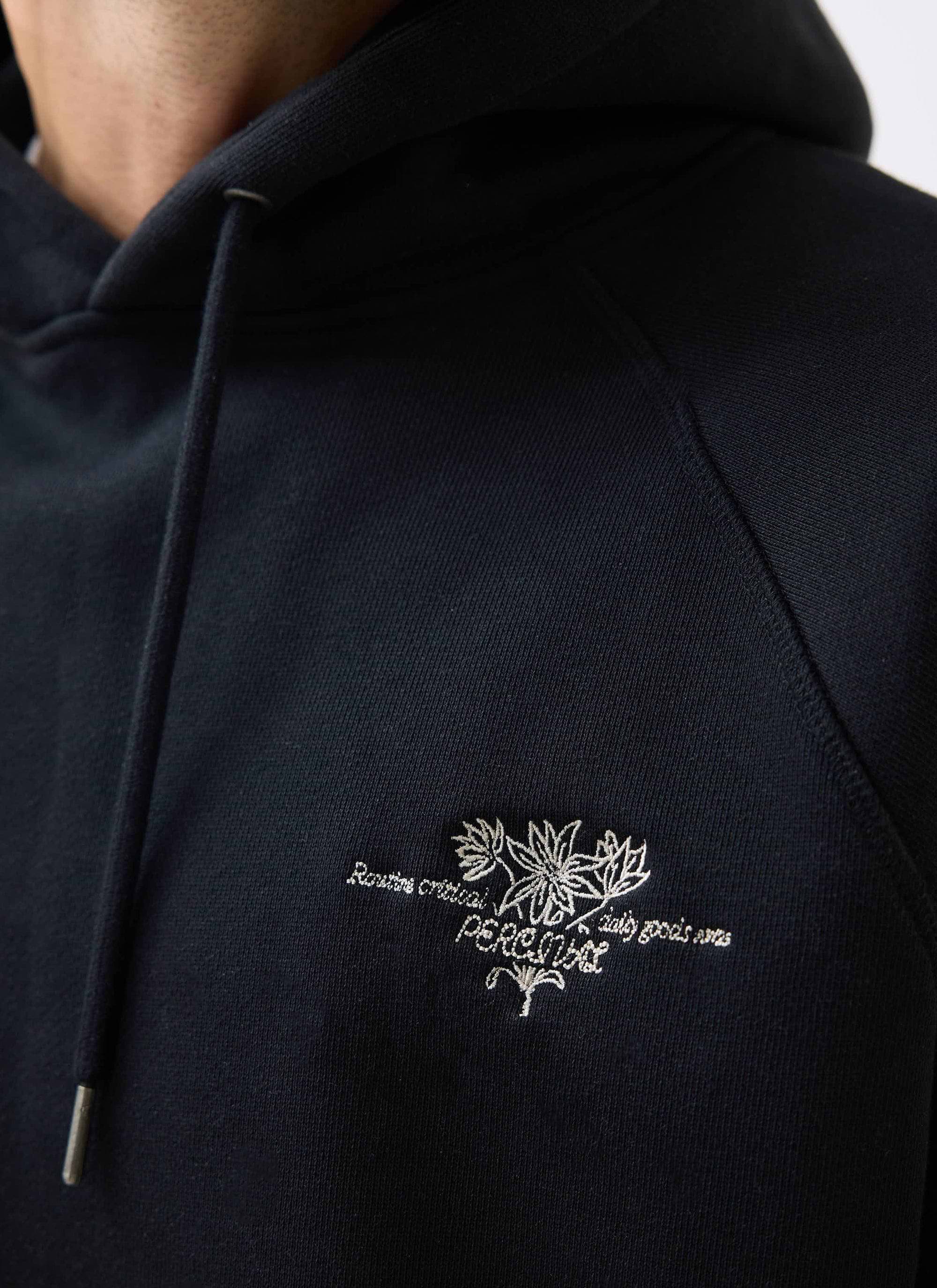 A close-up of the intricate floral embroidery on the chest of the black Heritage 90's Raglan Hoodie from Percival.