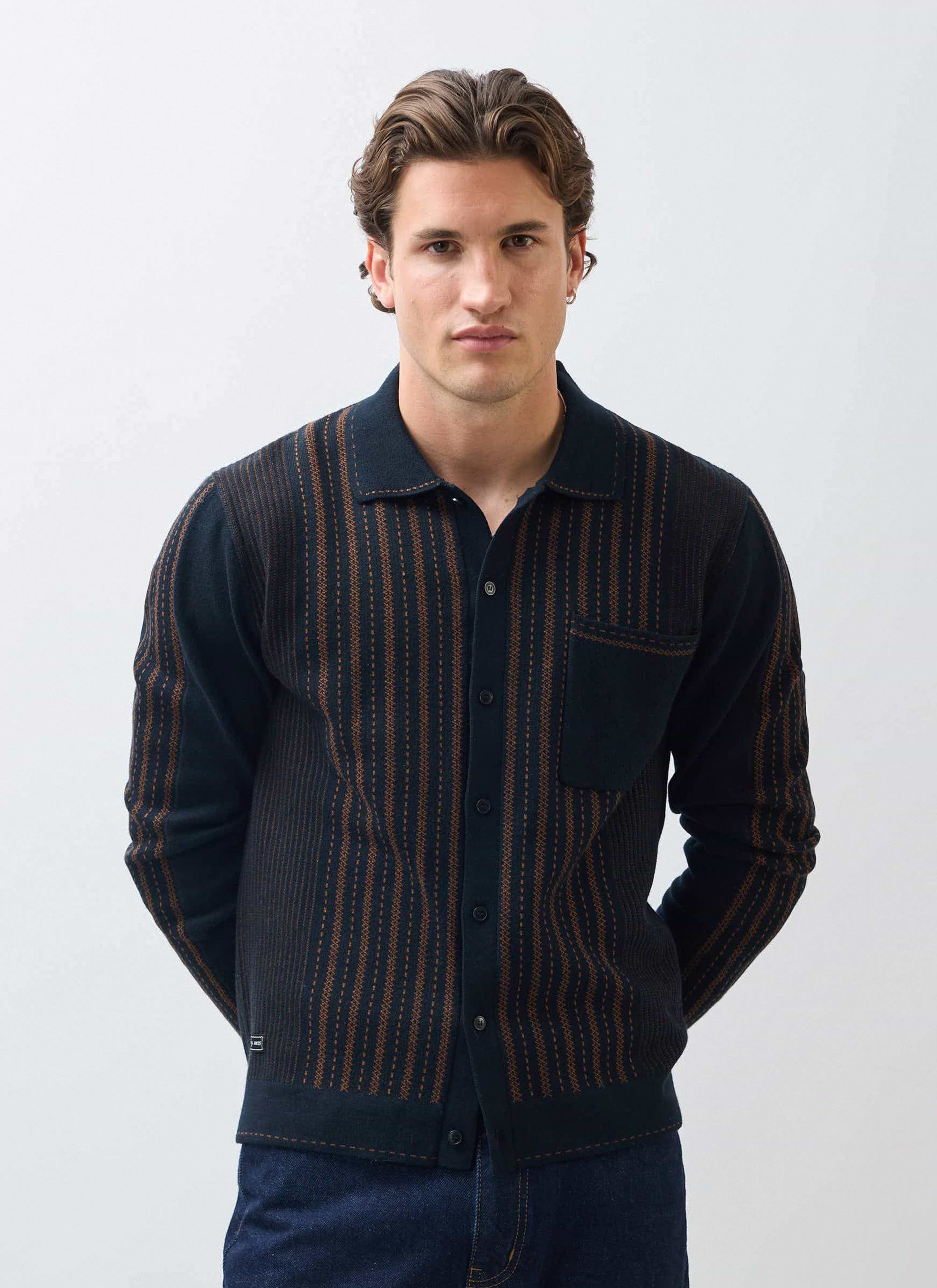 A model faces forward wearing the Percival Appendix jacquard knit shirt in black with vertical brown stripes.