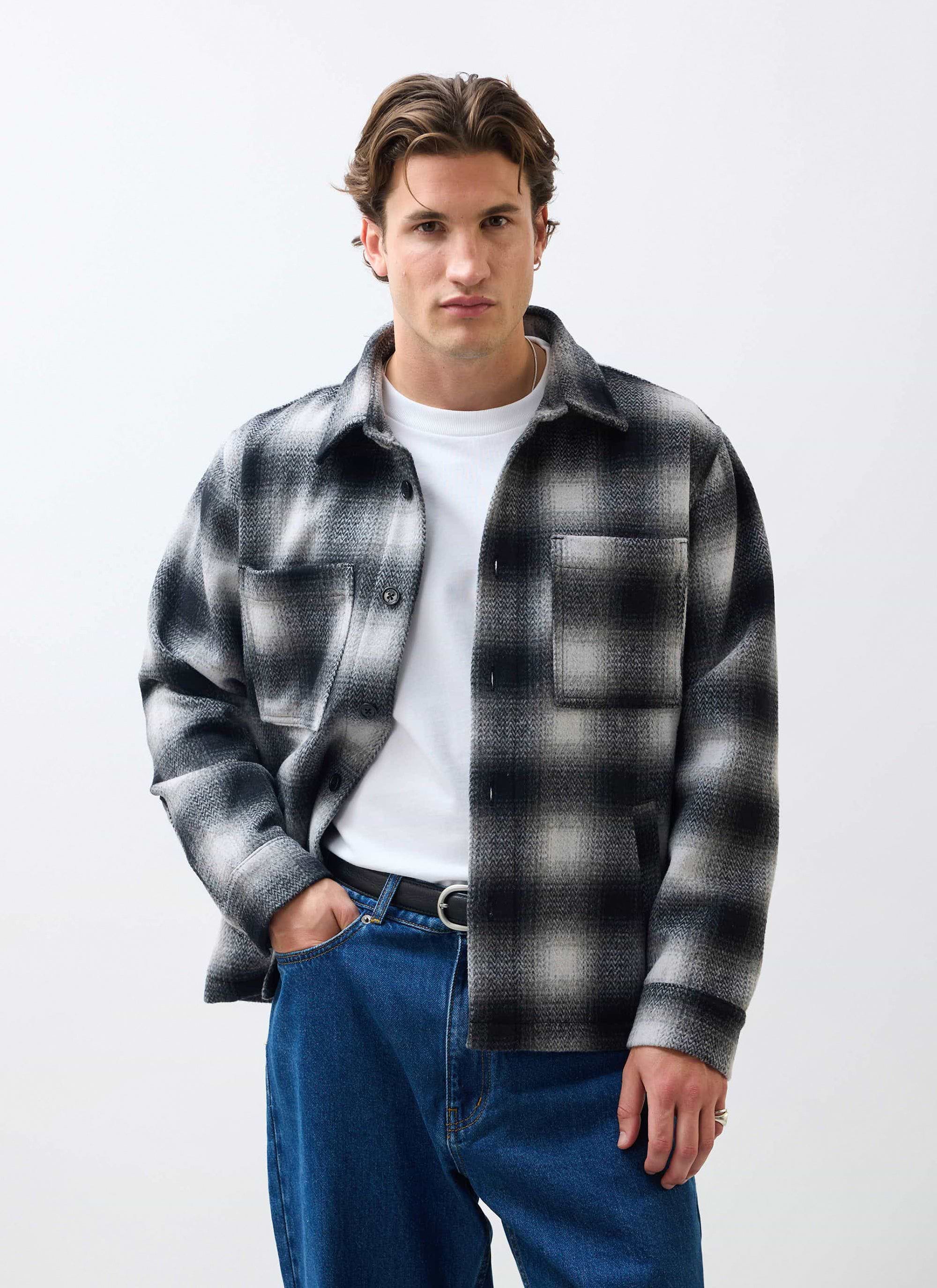 A man models the Percival Check Overshirt in grey, a wool-blend shacket styled over a white t-shirt and dark jeans.