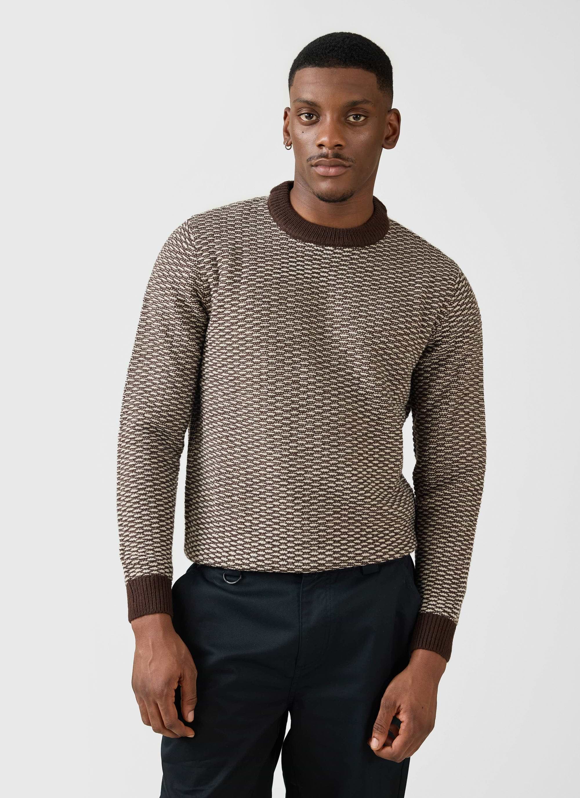 A model wears the Percival Charlestown Knitted Jumper in chocolate and beige, a textured crewneck styled with black trousers.