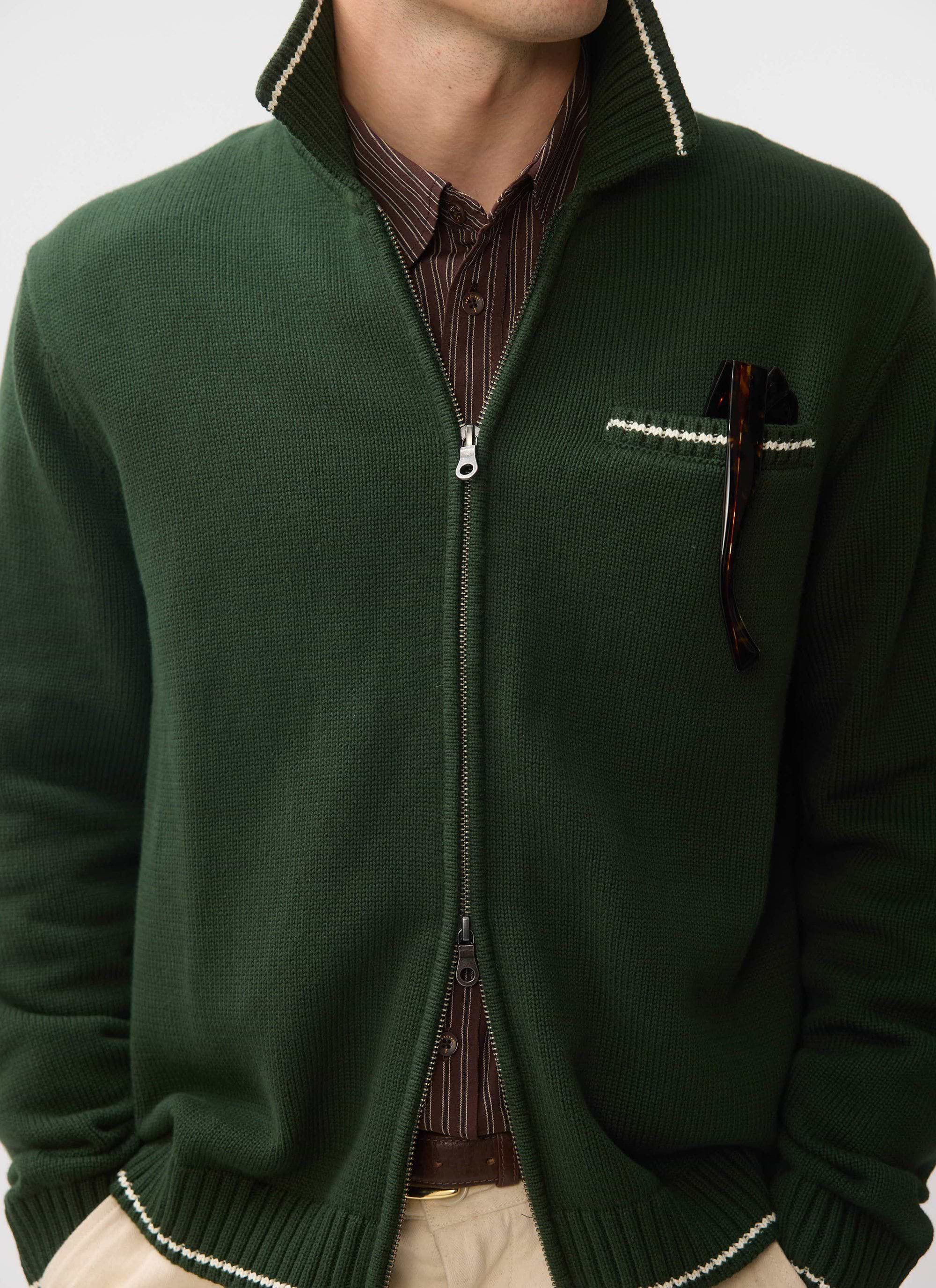 A close-up of a model wearing the Percival Gardner zip cardigan in forest green, showing the contrast stitch details.