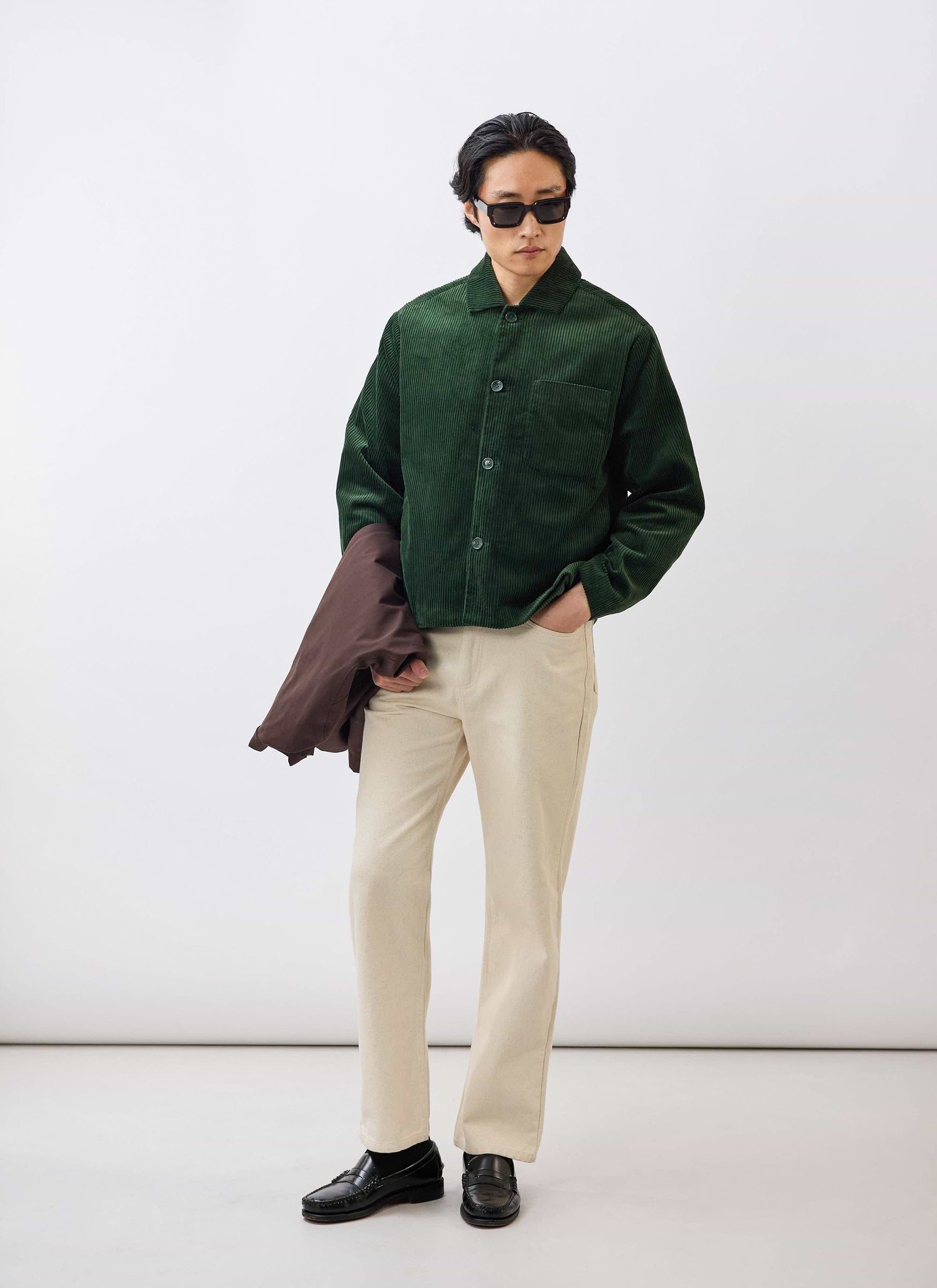 A model wears the Percival Cord Overshirt in forest green, styled with cream trousers, sunglasses, and black loafers.