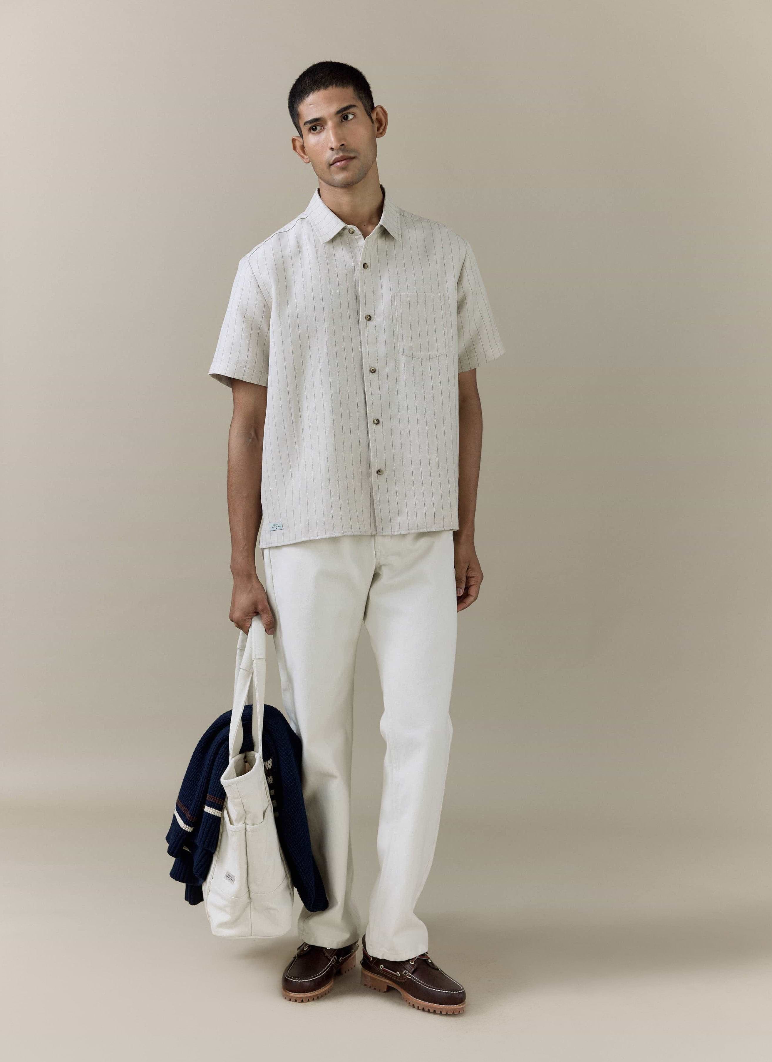 Model wearing the Percival Striped Boxy Shirt in cream pinstripe linen blend, styled with white trousers.