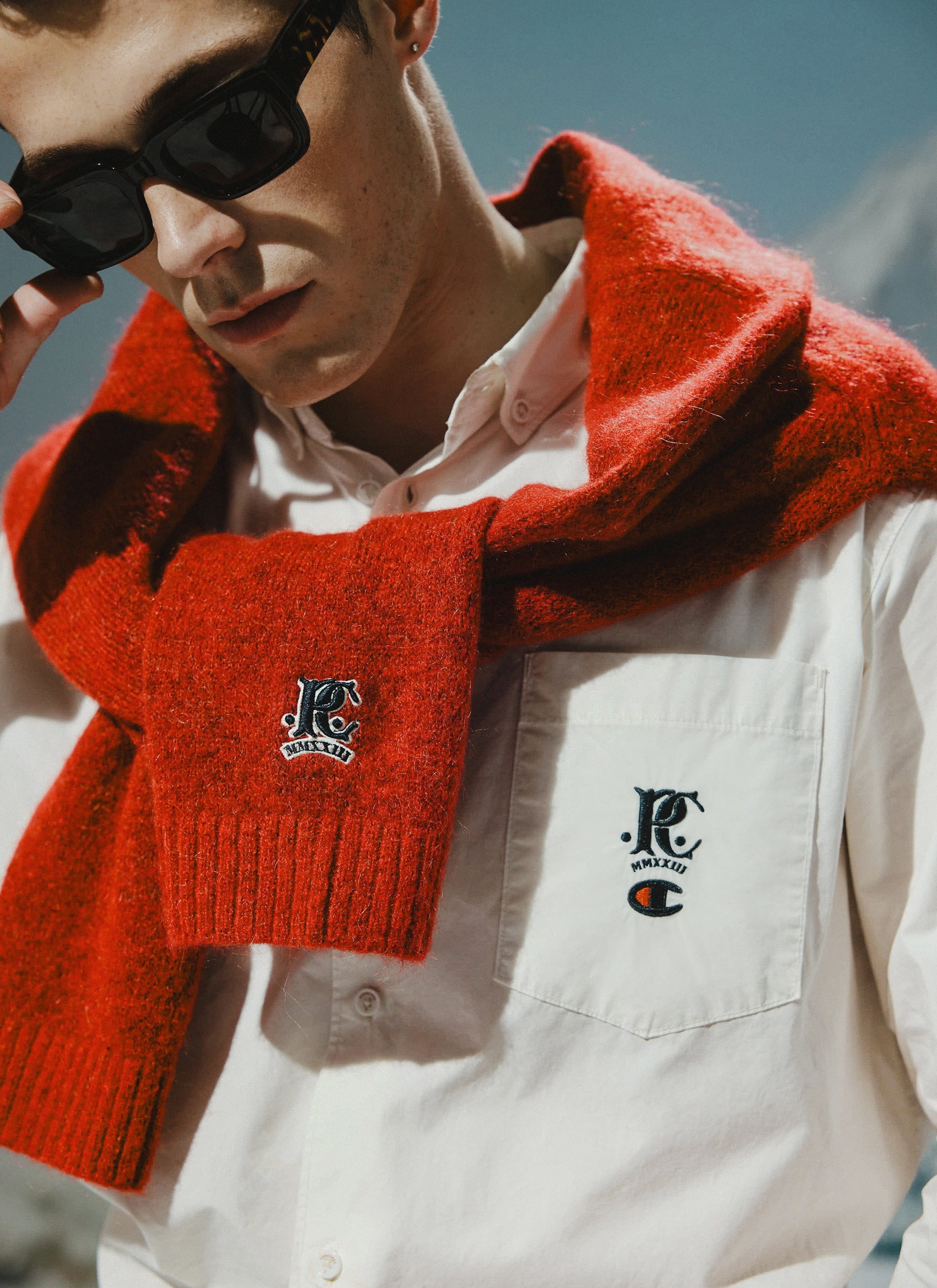 A model wears the Percival x Champion ecru shirt, with the red mohair cardigan draped to show the matching chest embroidery.