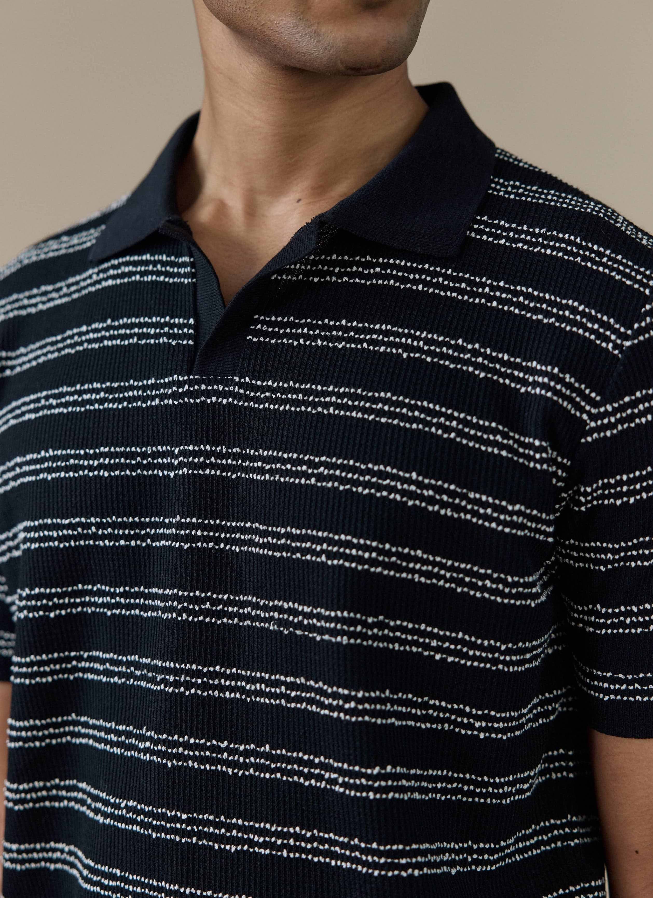 Close-up of the Percival Laurent Polo in black, showing the textured stripe stitch pattern and open collar design.
