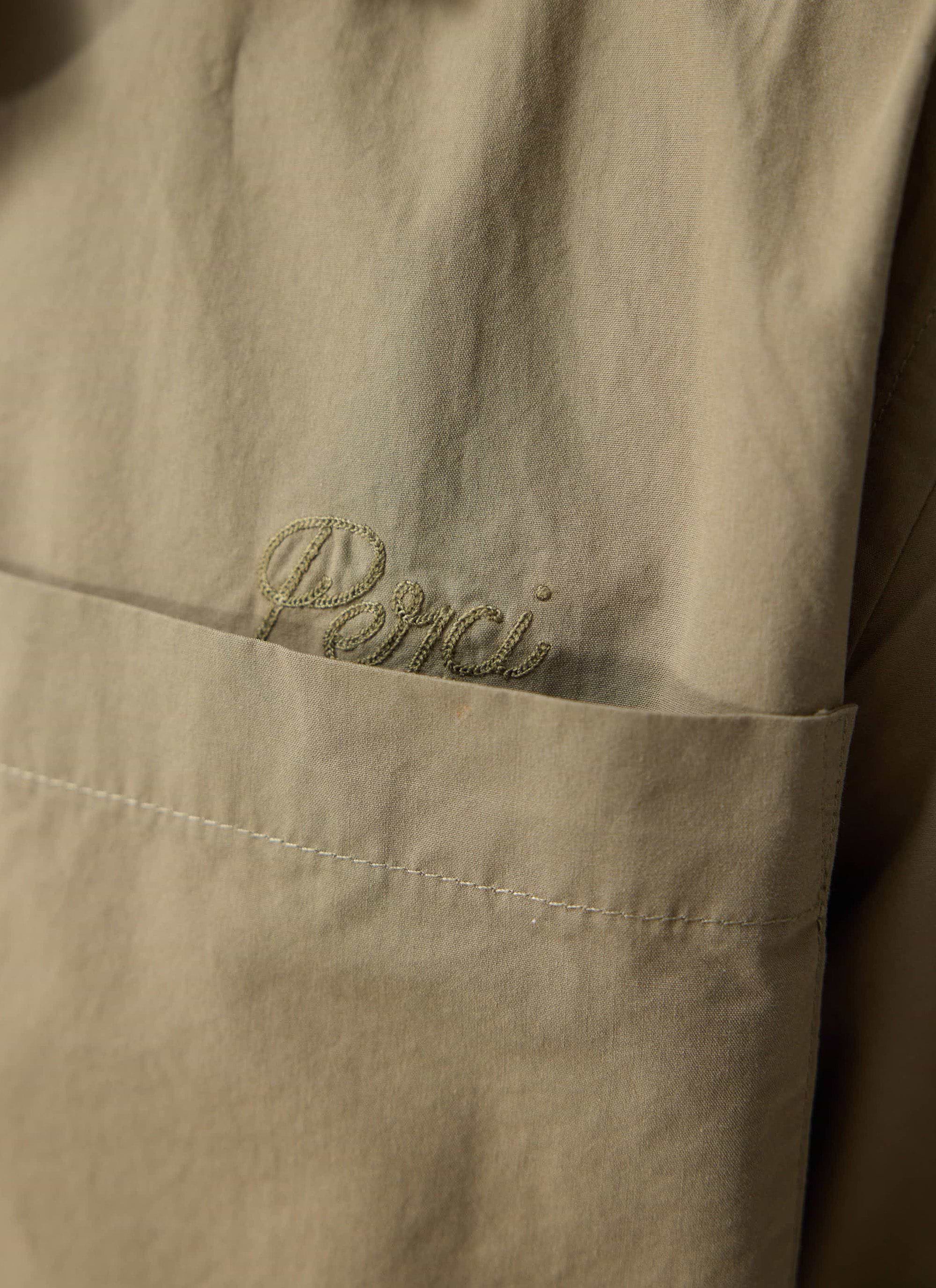 A close-up of the tonal 'Perci' embroidery on the chest pocket of the olive Boxy Cropped Cuban Collar Shirt from Percival.