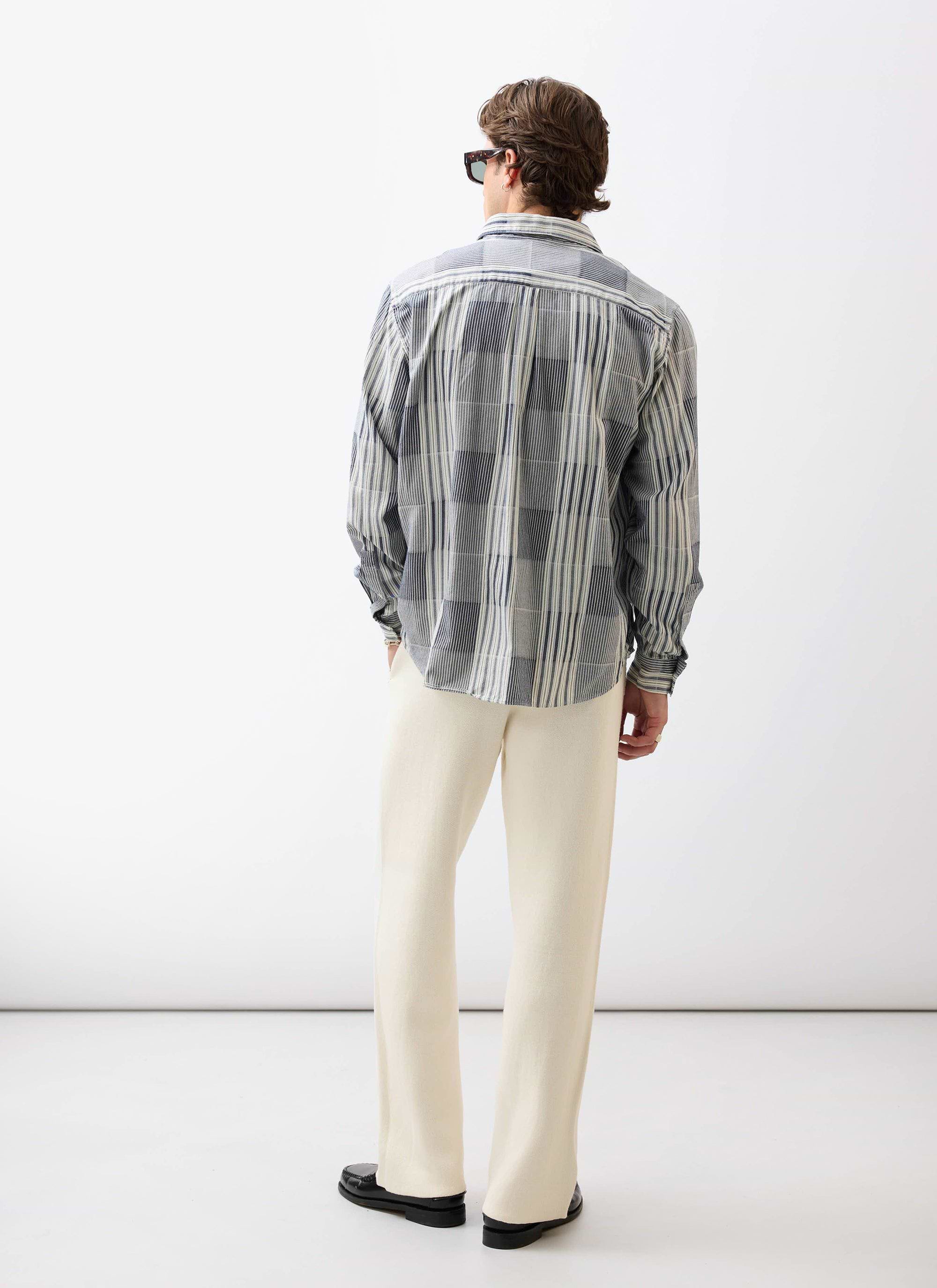 A model seen from the back wearing the Percival Epigraph Patchwork Pearce shirt in blue with cream trousers.