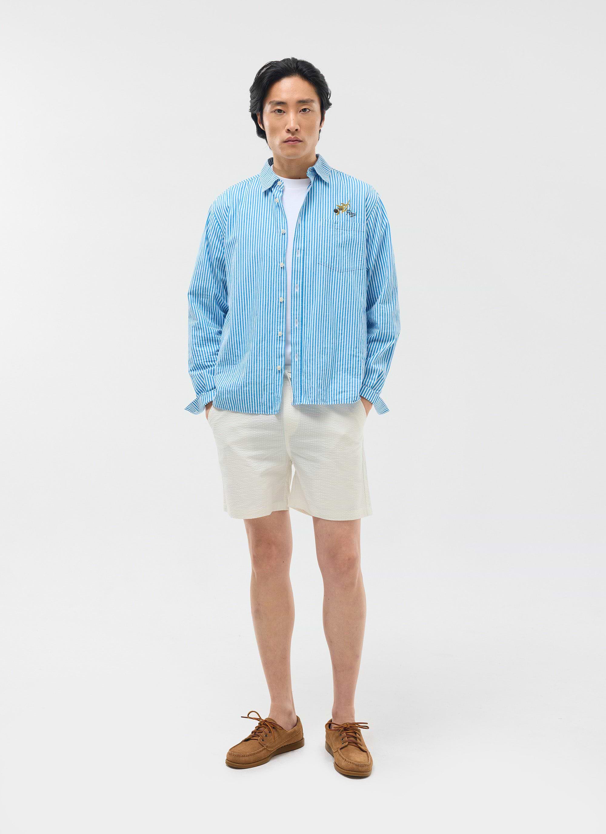 A model wears the Percival Classic Shorts in cream seersucker, styled with a blue striped shirt and brown shoes.