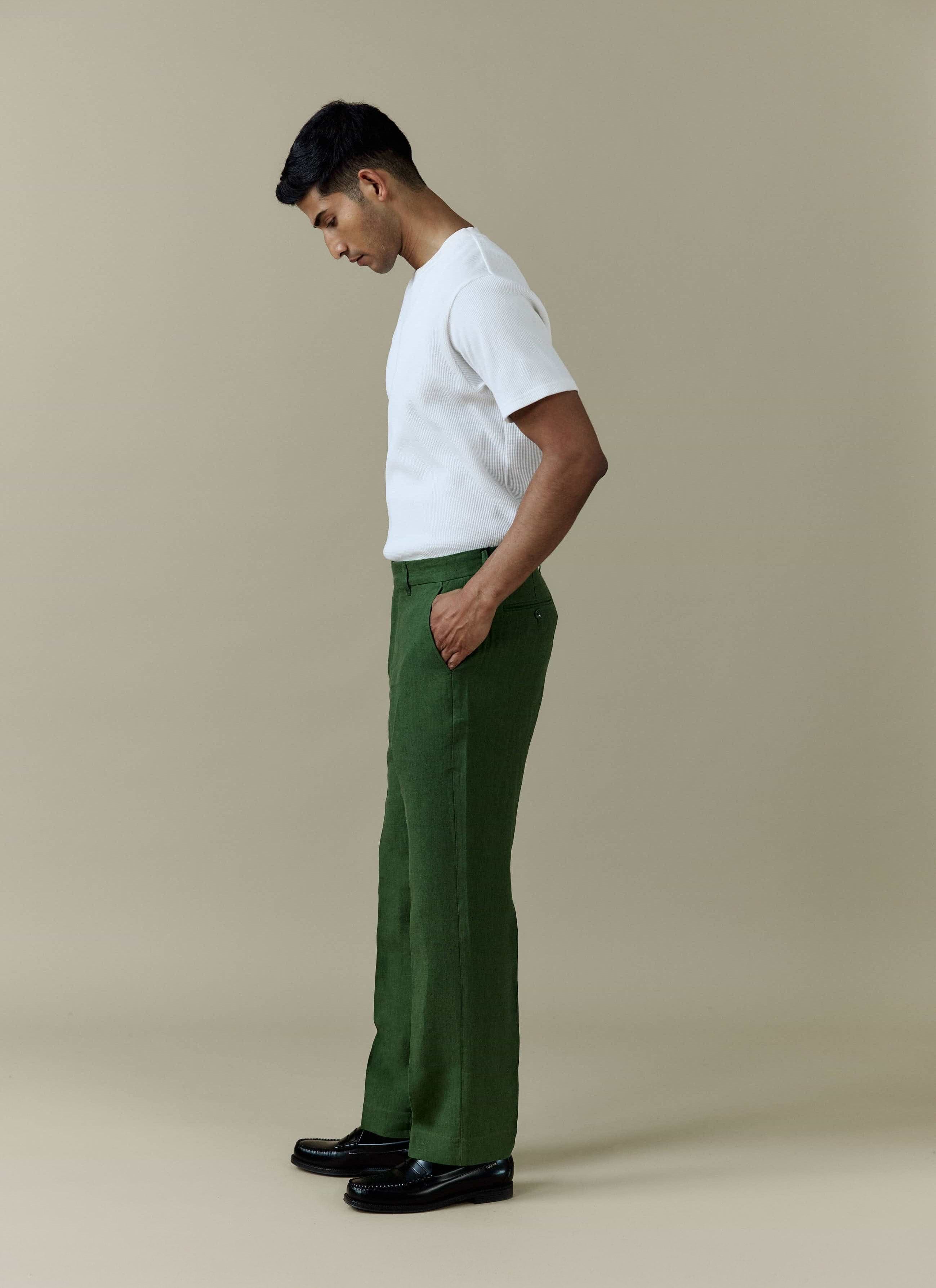 Side view of a model wearing Percival Tailored Linen Trousers in forest green with a white t-shirt and black loafers.