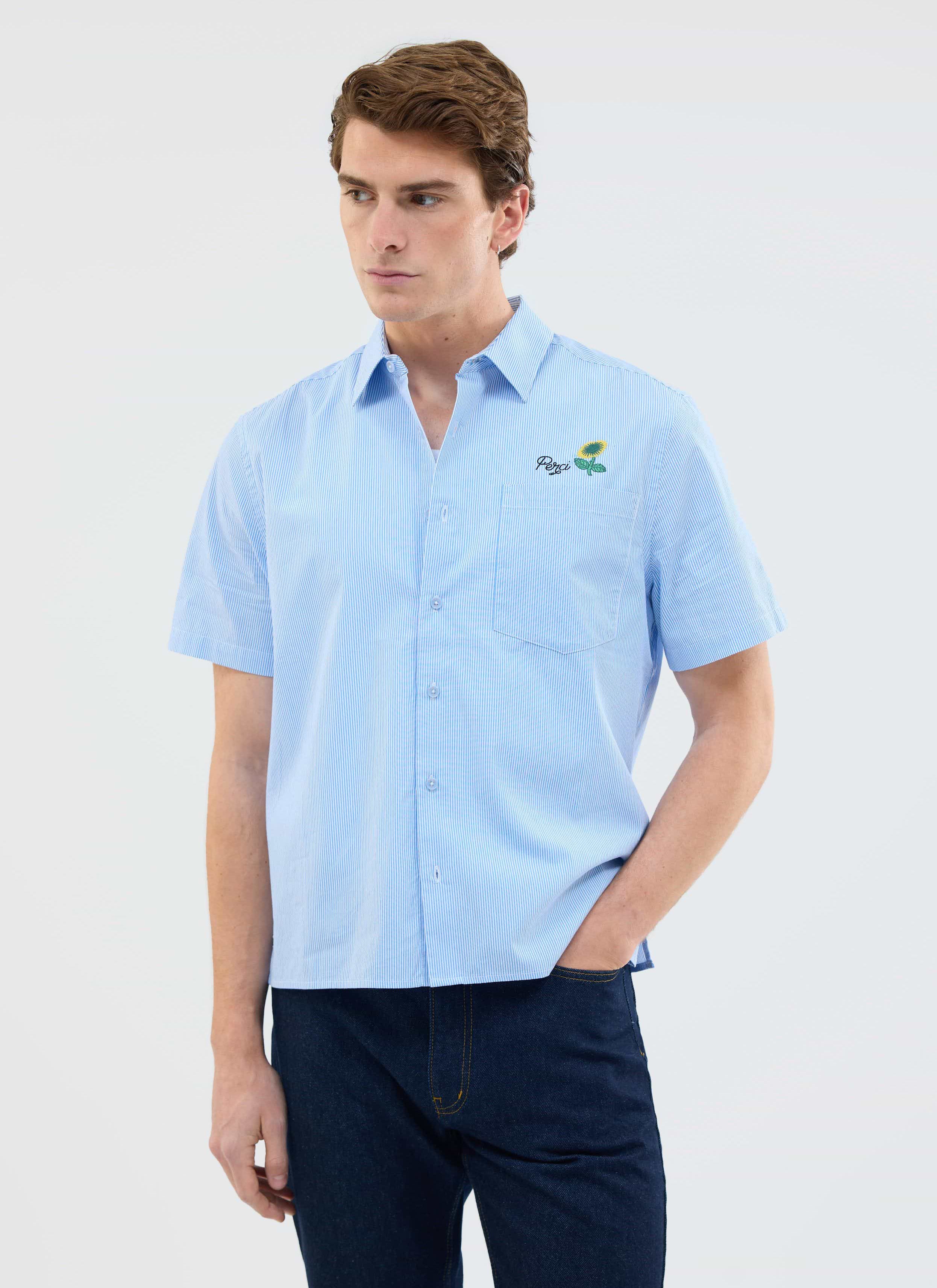 A man models the Percival Sunflower Stripe Shirt in a blue pinstripe, showing the signature sunflower chest embroidery.