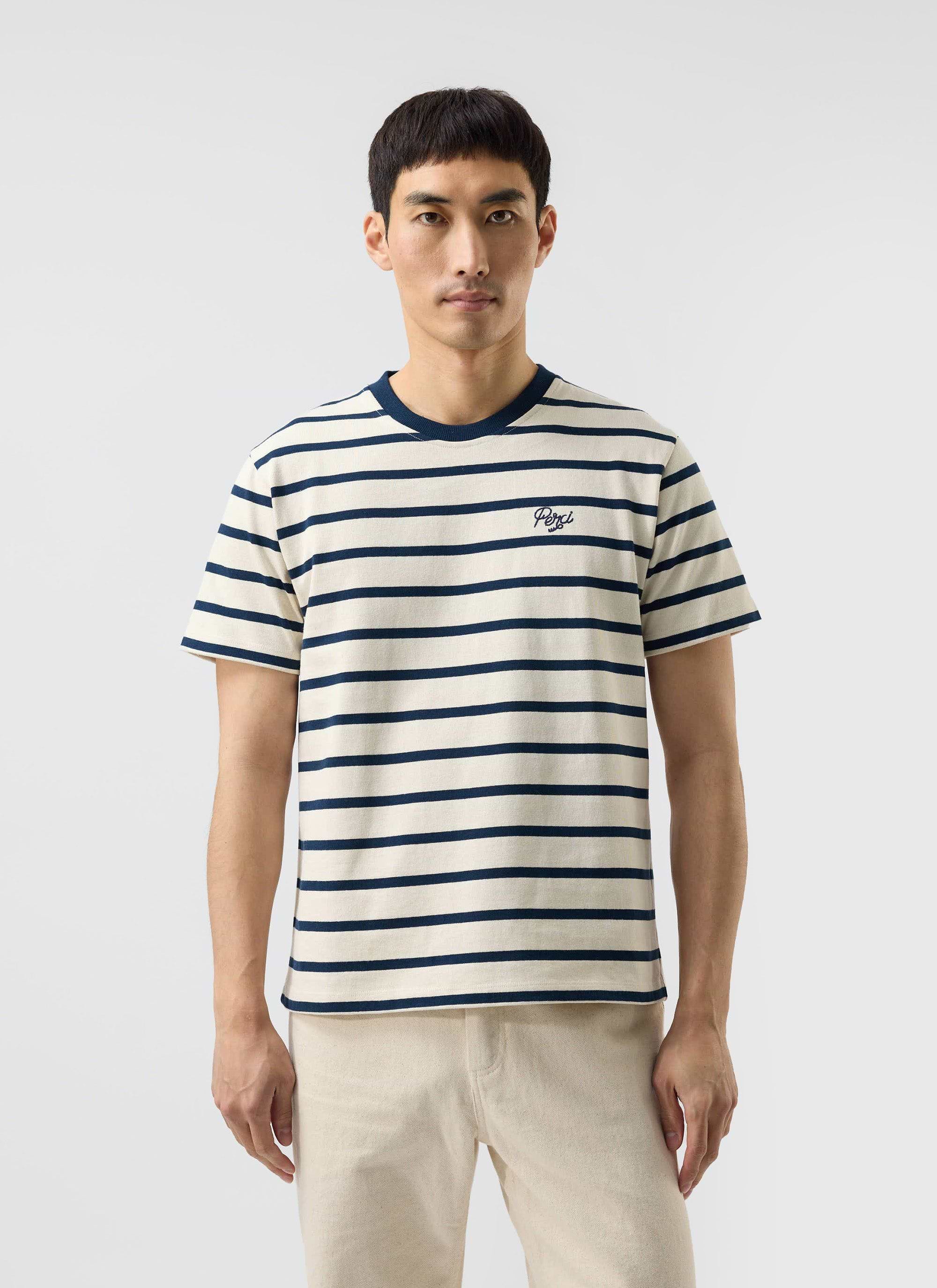 A man models the Percival Breton Stripe T-shirt in ecru and navy against a plain white studio background.