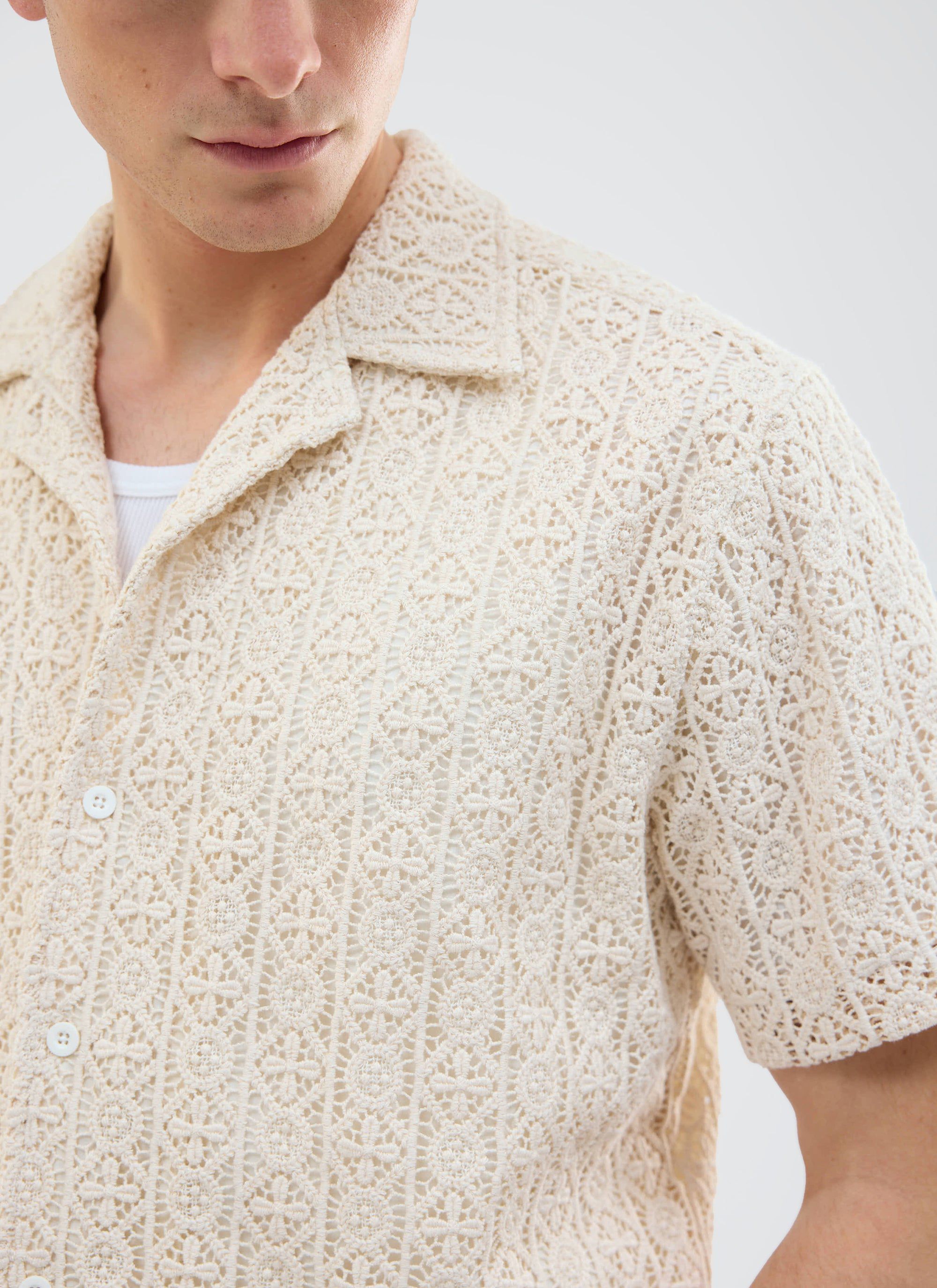 A close-up of a model wearing the ecru Elio Crochet Cuban Shirt from Percival, showing the intricate pattern detail.