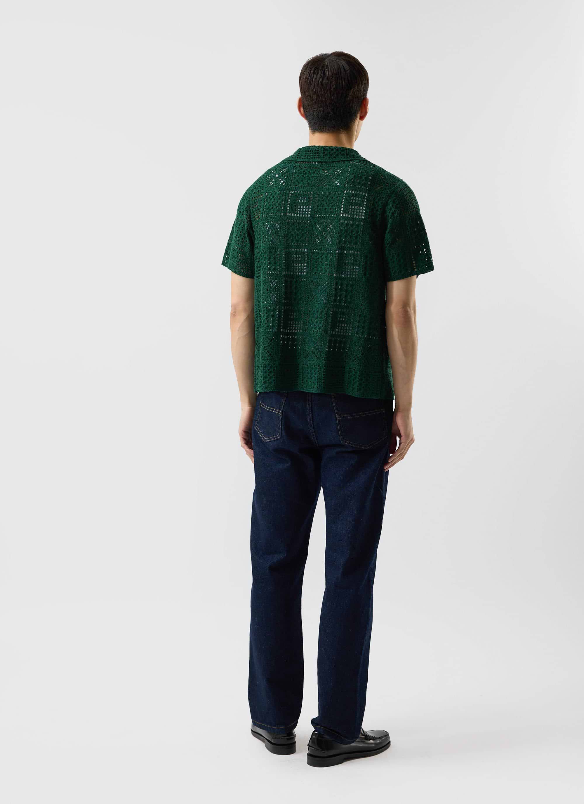 A rear view of a model wearing the Percival Crochet Groundsman Shirt in forest green with dark wash jeans.