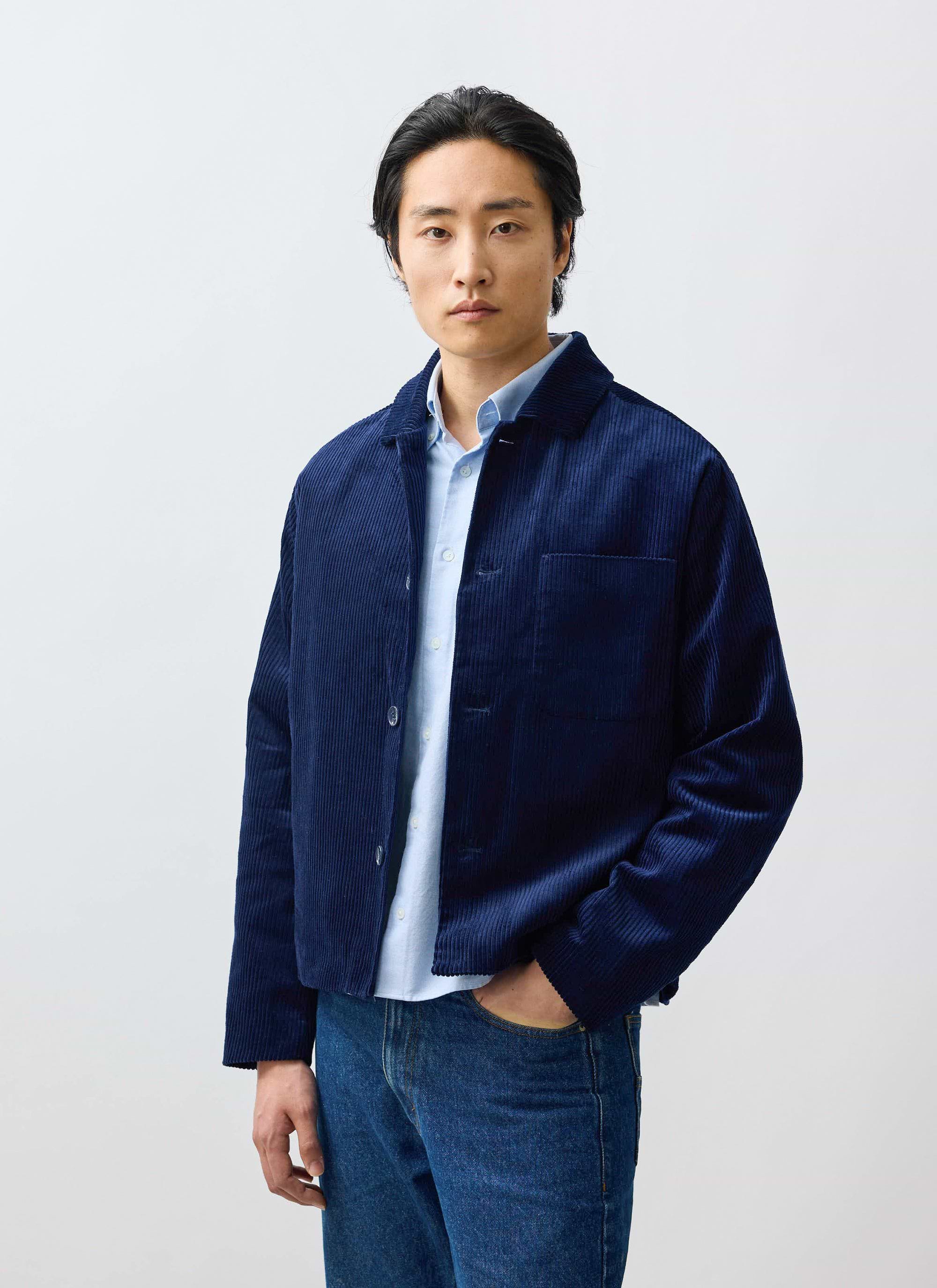 A model wears the Percival Cord Overshirt in navy, layered over a light blue shirt and styled with denim jeans.