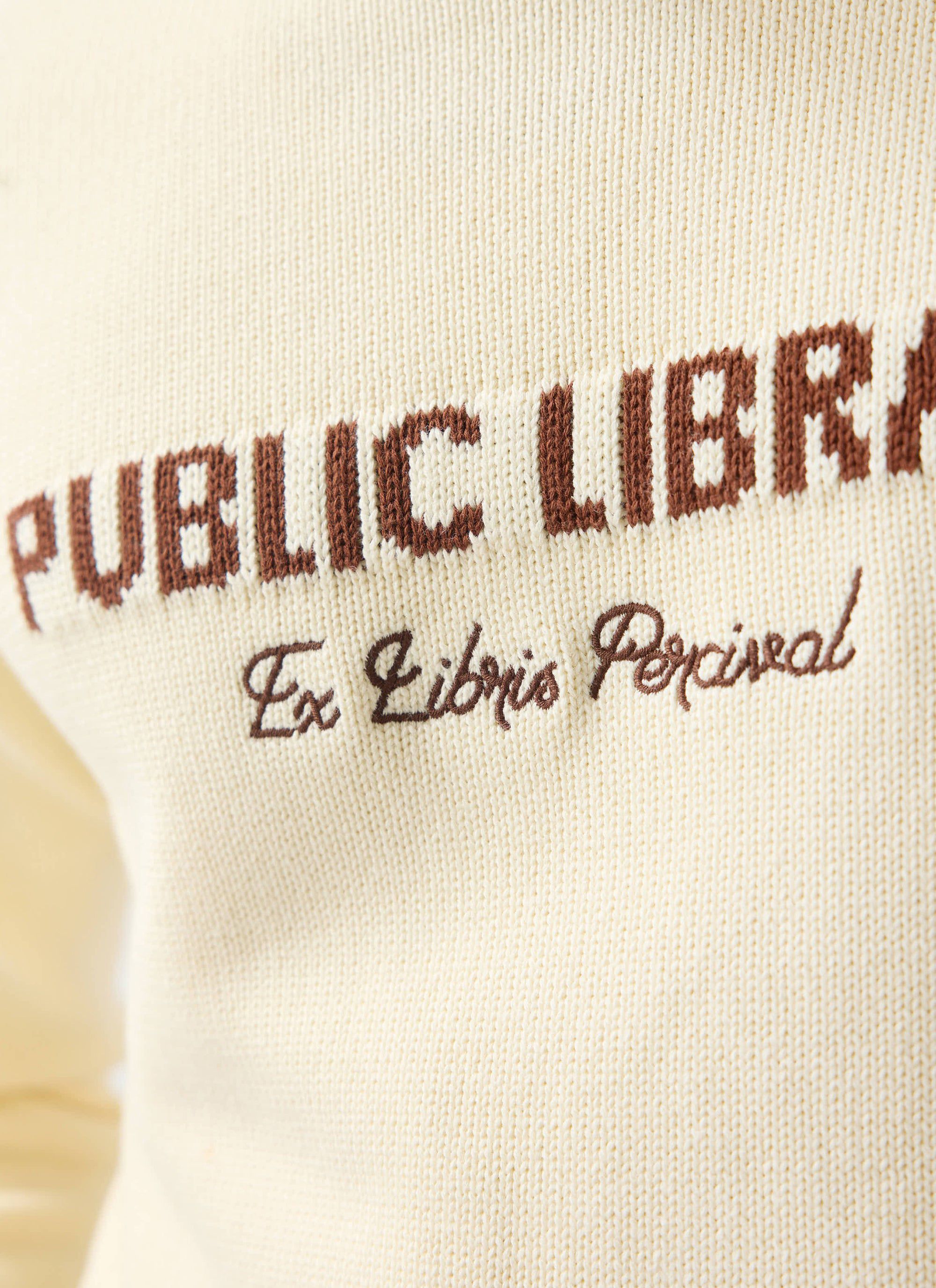 A close-up of the ecru cream Public Library Knitted Jumper, showing the brown 'Ex Libris Percival' chest embroidery.