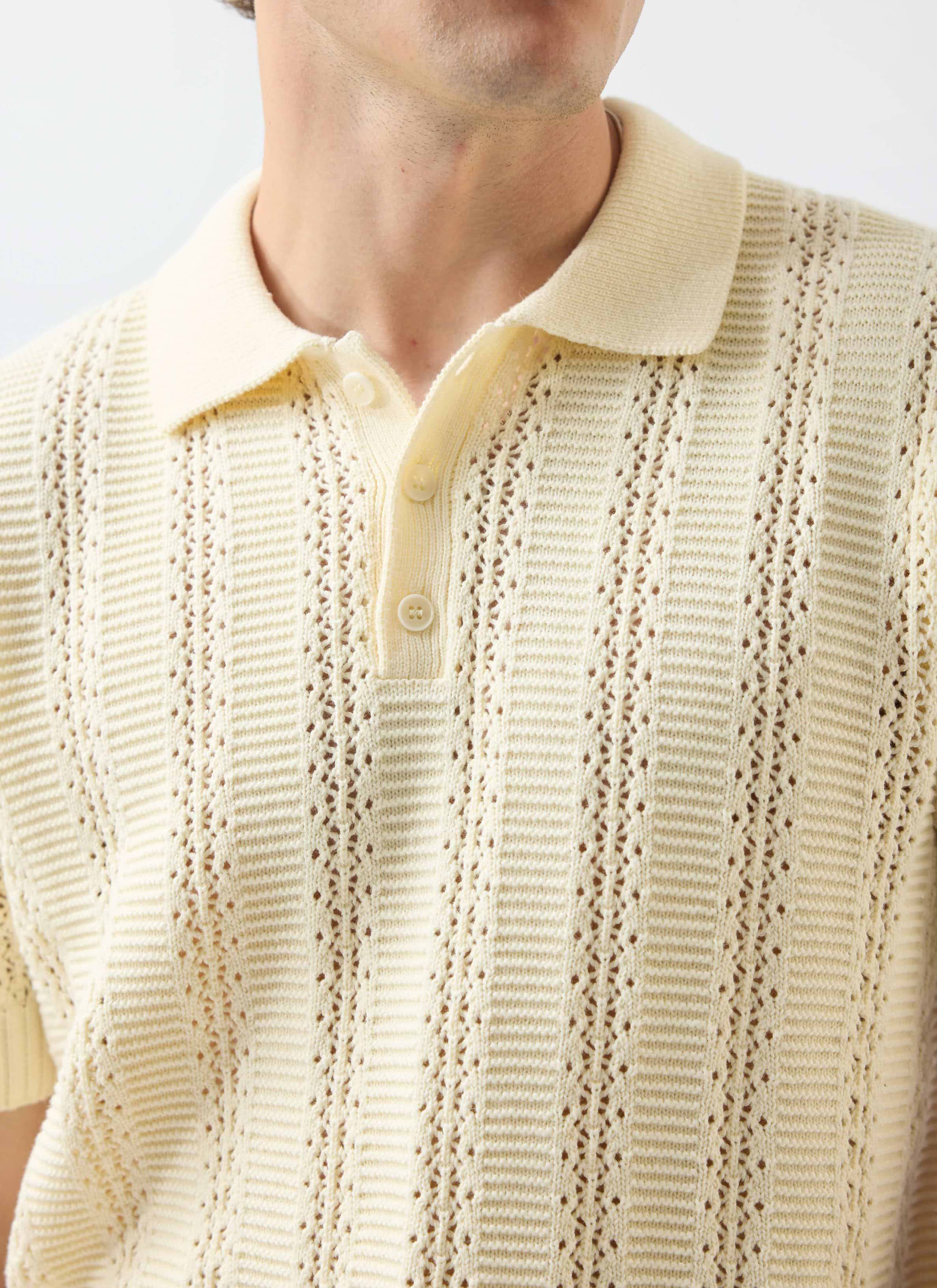 A close-up of a model wearing the Percival Addendum Knitted Polo Shirt in ecru, showing the detailed jacquard knit.
