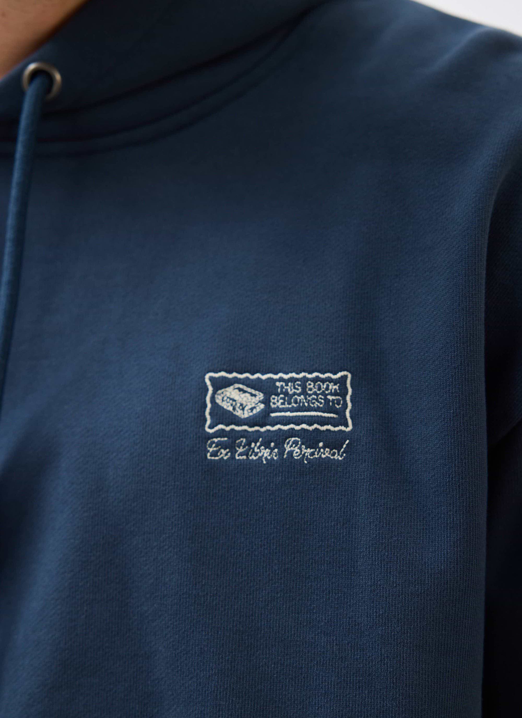 A close-up of the 'This Book Belongs To' and 'Ex Libris Percival' embroidery on the navy blue hoodie.