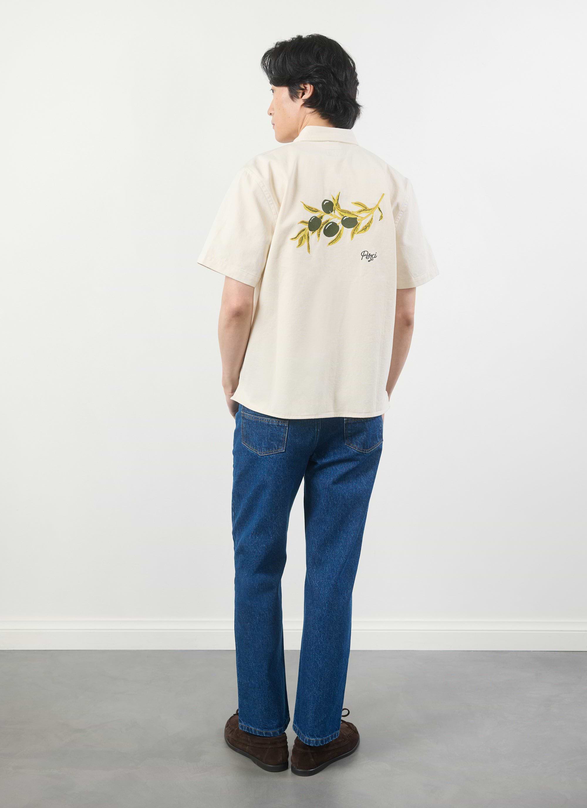 A man models the Percival Olive Embroidered Cropped Shirt in white, viewed from behind to display the olive branch graphic.