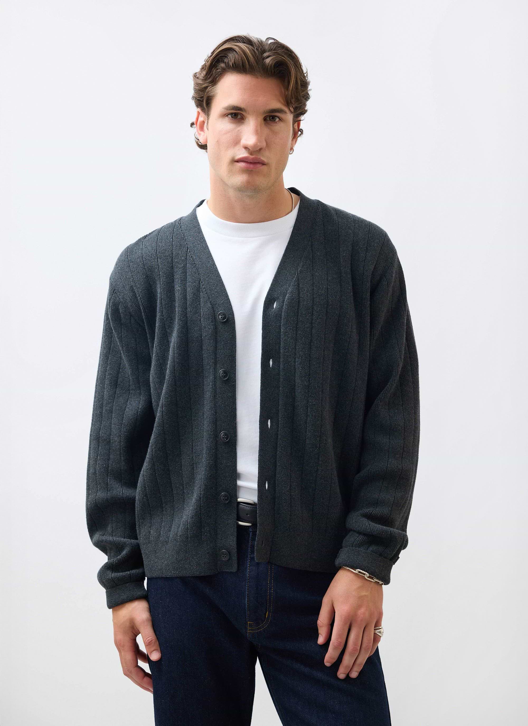 A model wears the Percival Editor Cardigan in grey, a ribbed cotton-wool blend knit, over a white t-shirt and jeans.