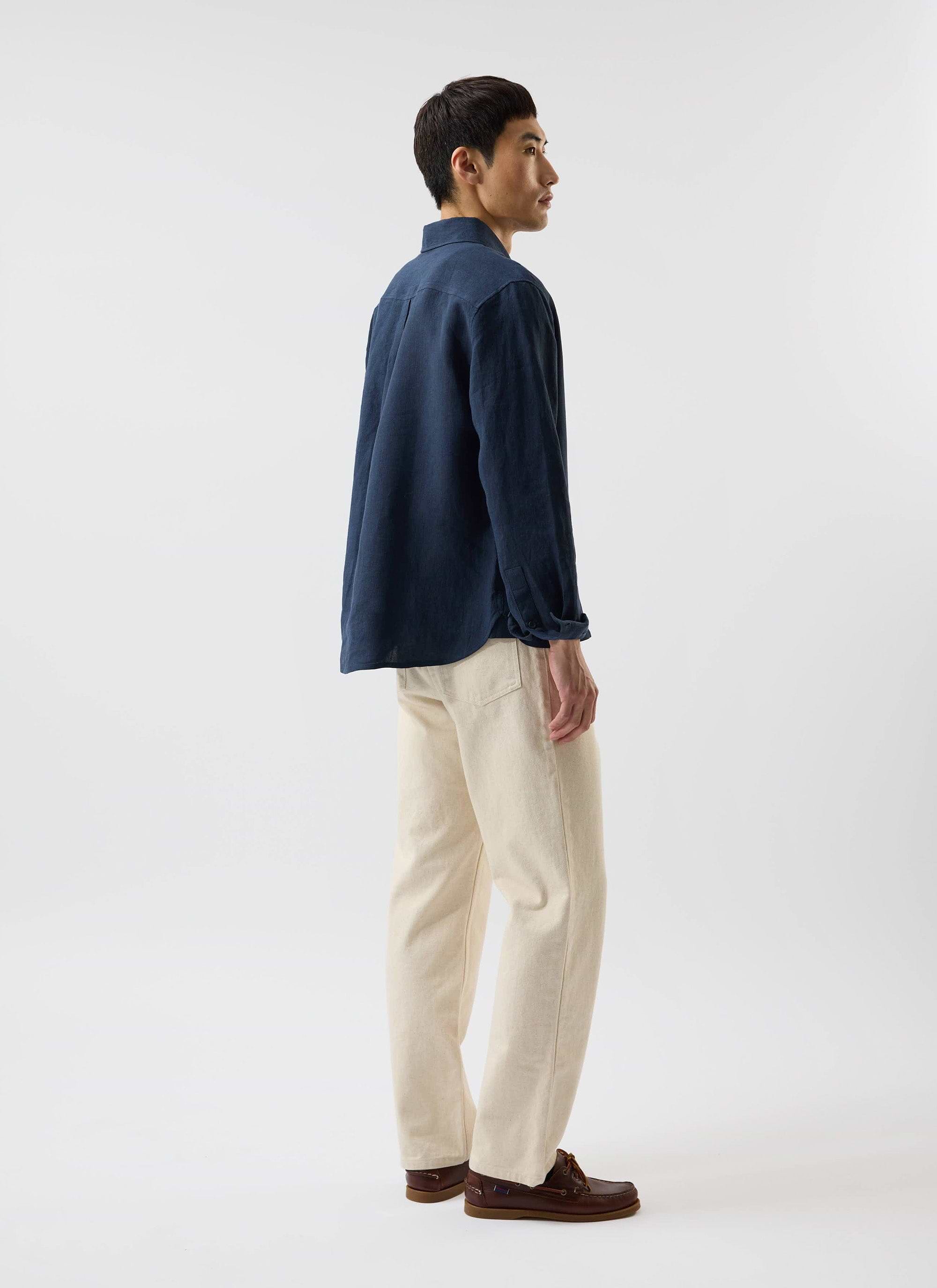 A man models the navy linen Pearce Shirt by Percival, paired with cream trousers and brown boat shoes.