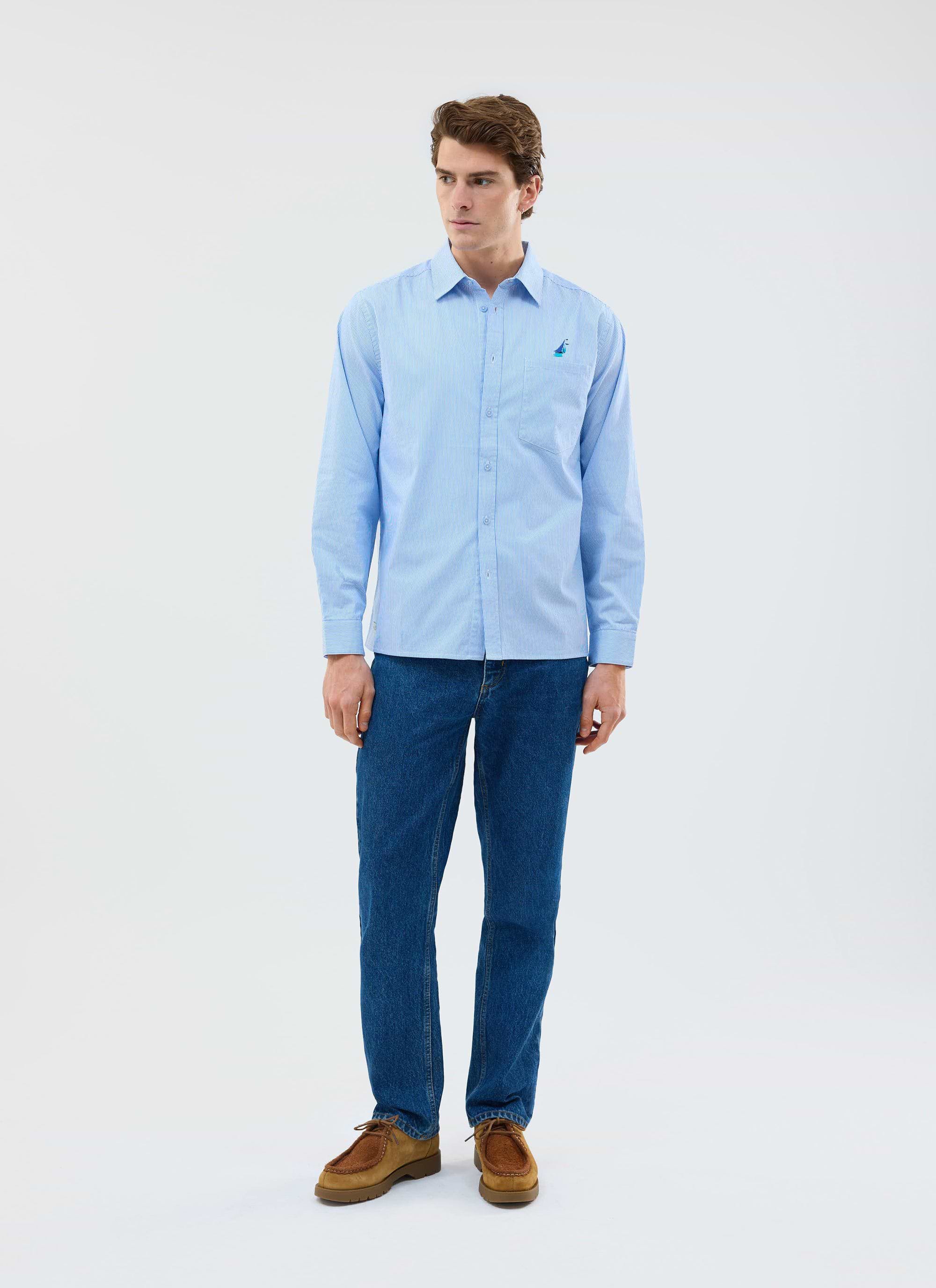 A man models the Percival Yacht Stripe Oversized Shirt in blue, paired with dark wash jeans in a studio.