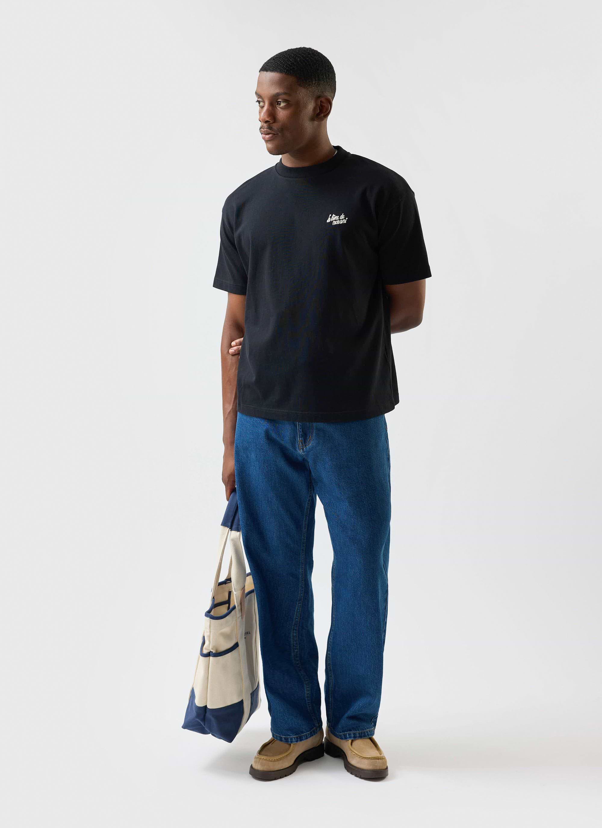 A model wears the Percival Le Livre De Mon Ami oversized t-shirt in black, styled with blue jeans and a tote bag.