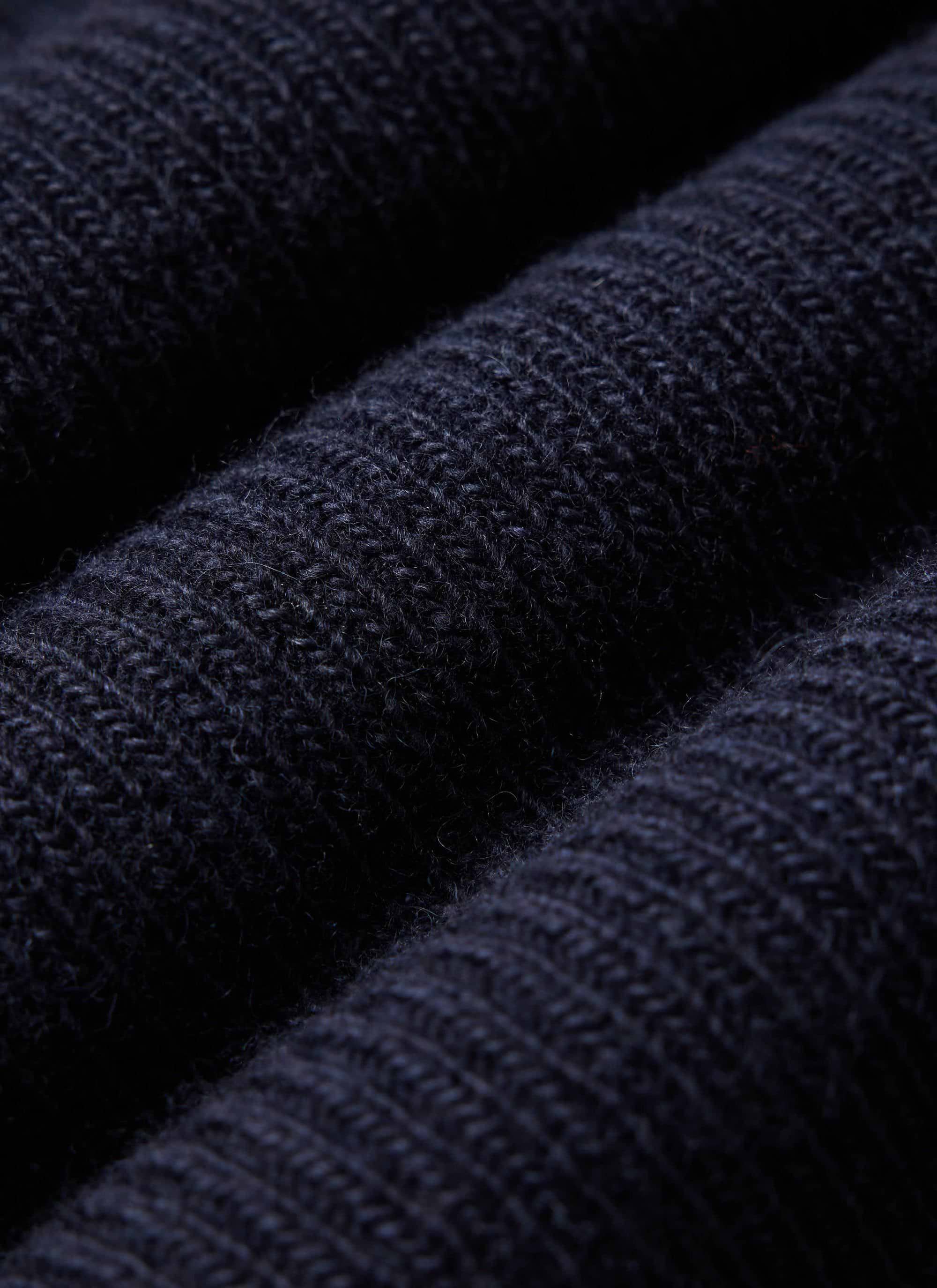 A close-up of the Percival Fisherman Raglan Jumper in navy, highlighting the chunky ribbed texture of the 100% wool knit.