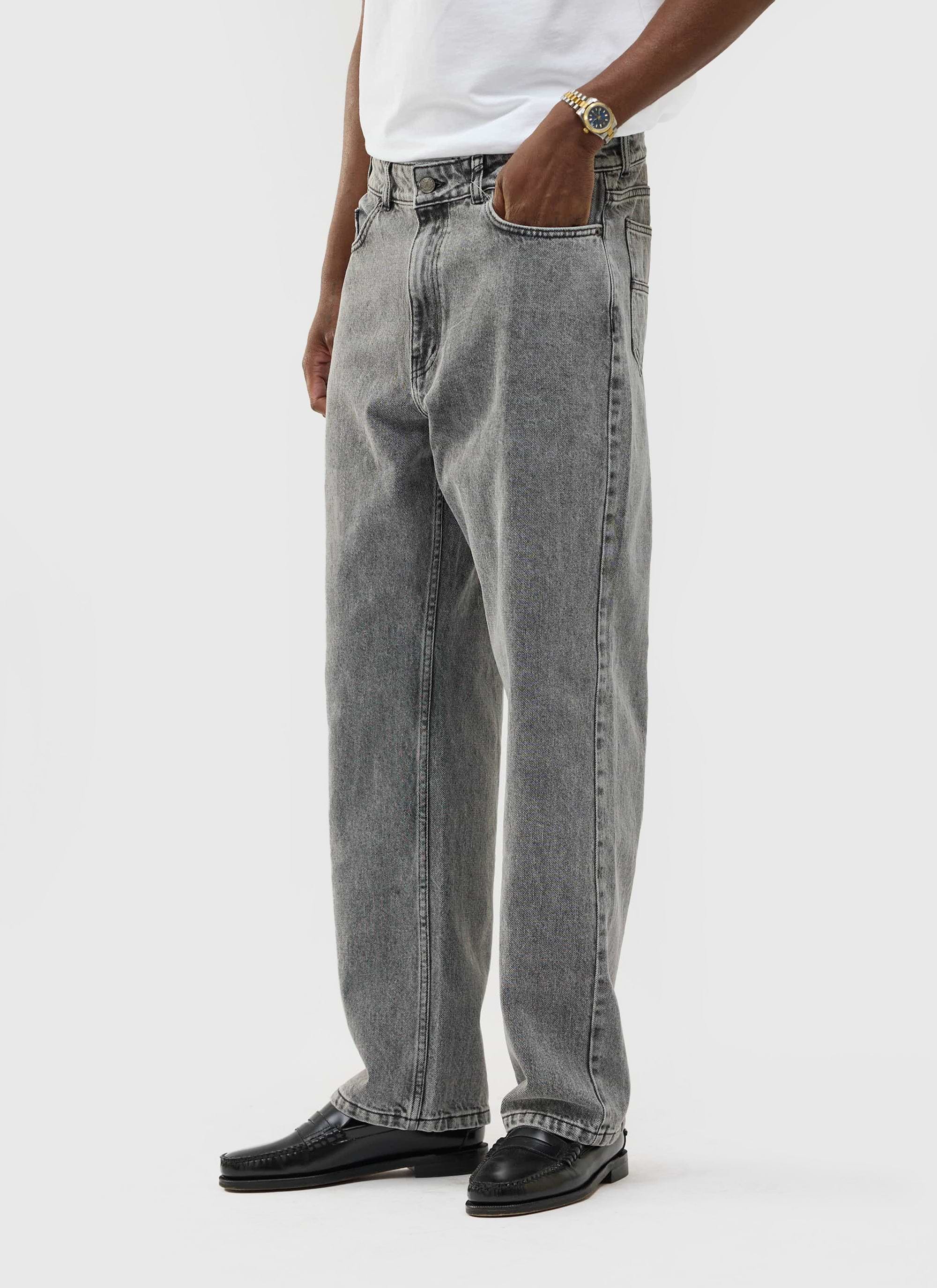 A model wears the Percival Wide Leg Denim Jeans in warm grey wash with a white t-shirt and black loafers.