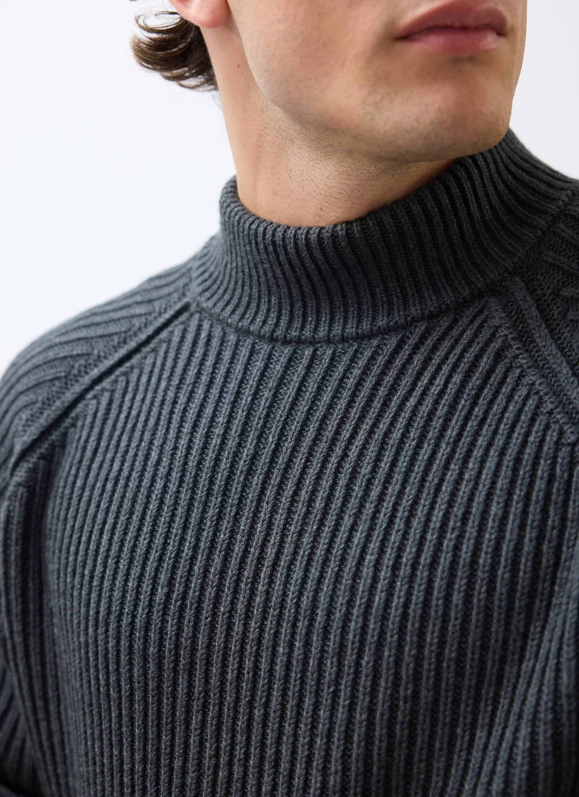 A close-up of a model wearing the Percival Library Turtle Neck in charcoal, showing the ribbed knit and shoulder detail.