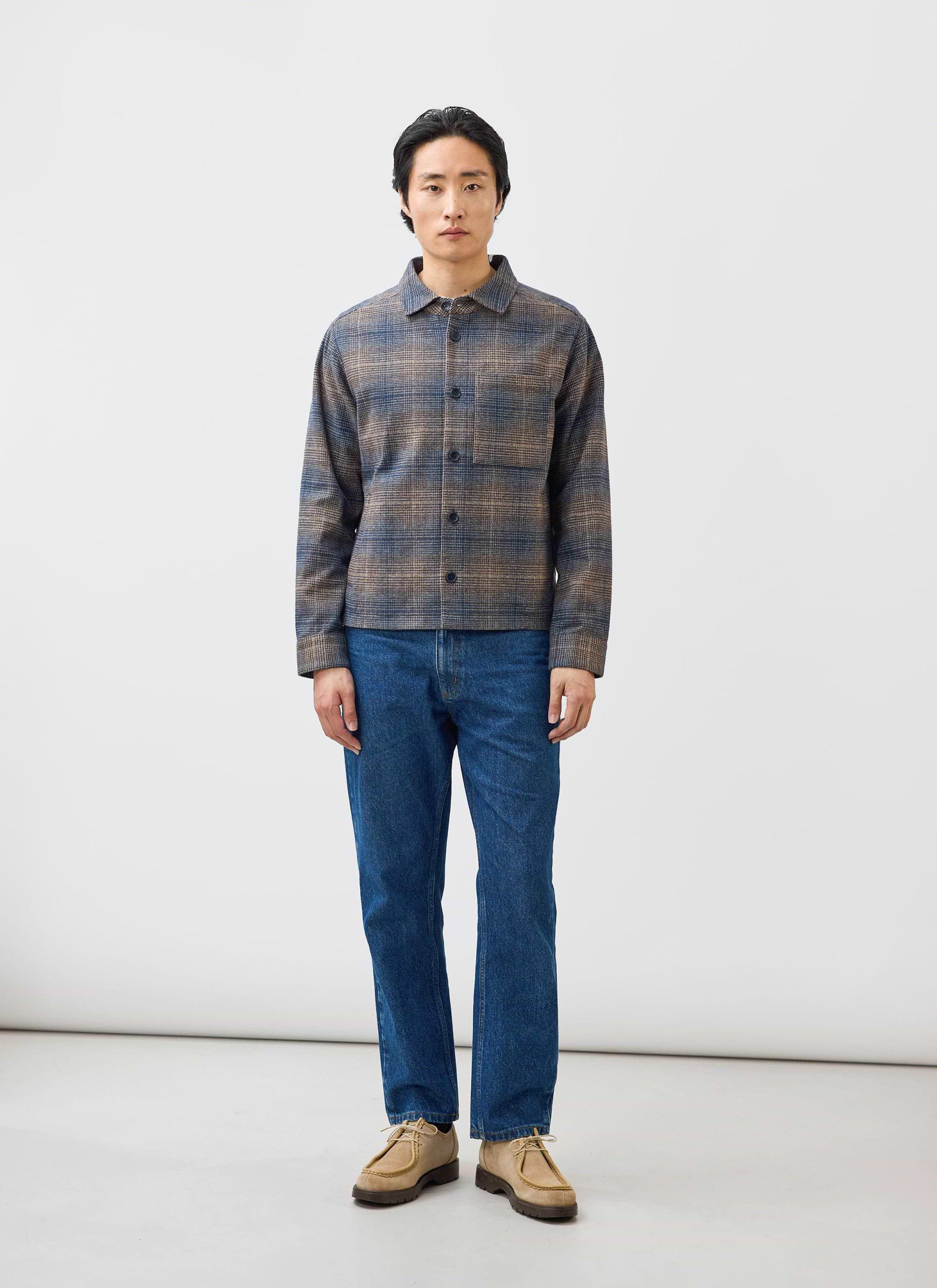 A model wears the Percival Luton Check Overshirt in brown, styled with blue jeans and tan shoes in a studio setting.