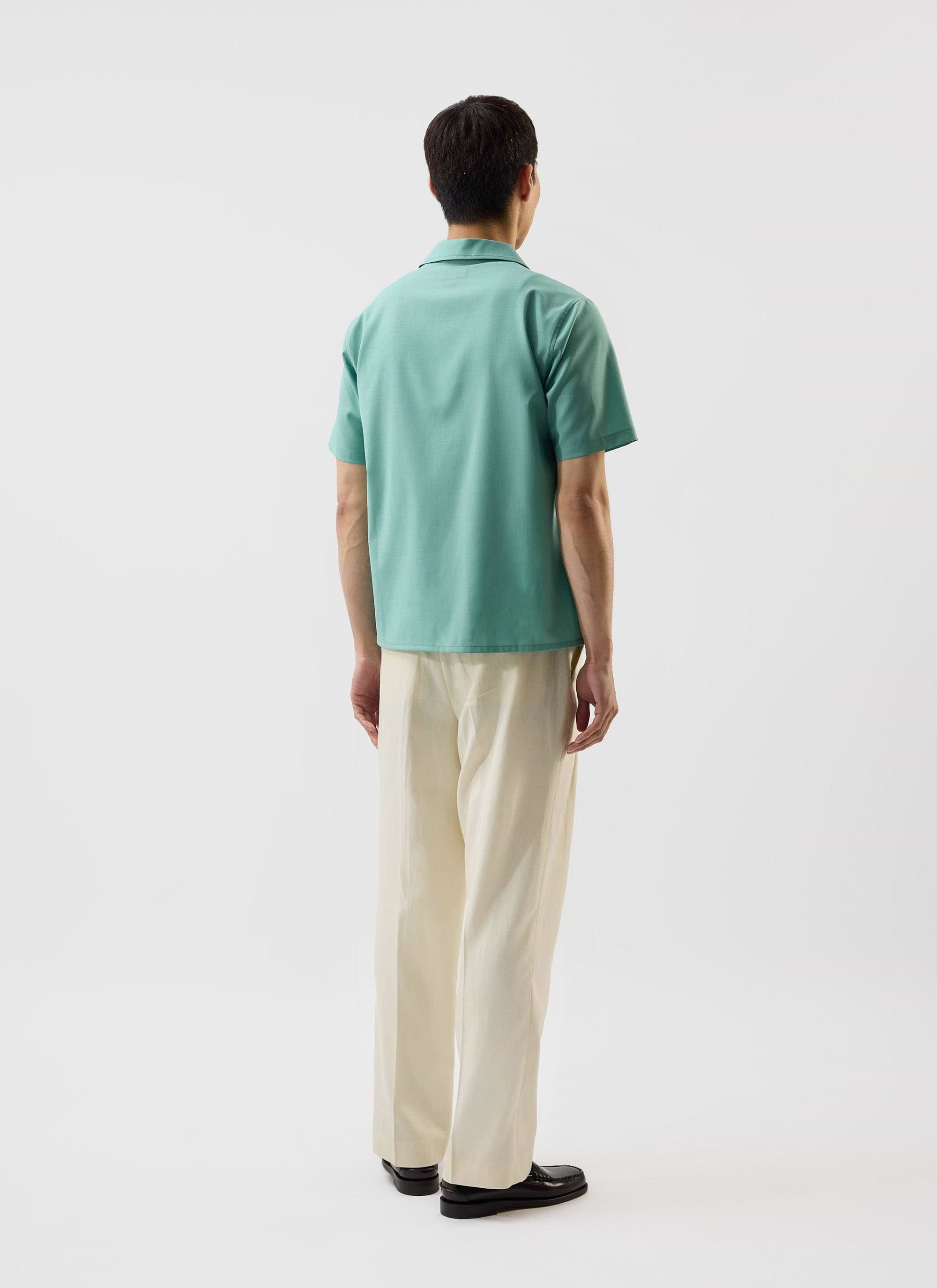 A model, seen from behind, wears the mint green Percival x Warren Drape Cuban Shirt with cream trousers.