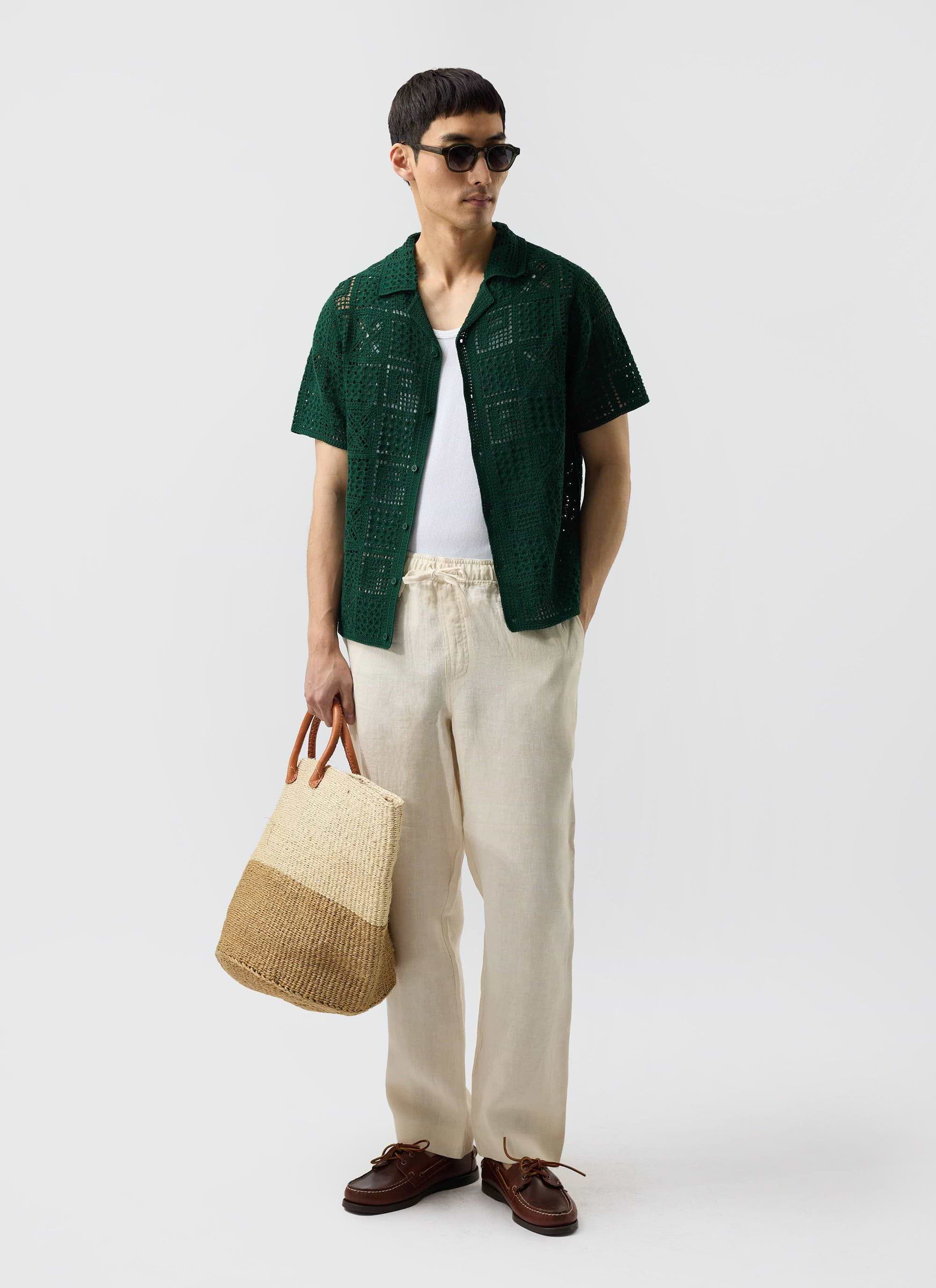 A model wears the Percival Crochet Groundsman Shirt in forest green over a white vest with ecru trousers and sunglasses.