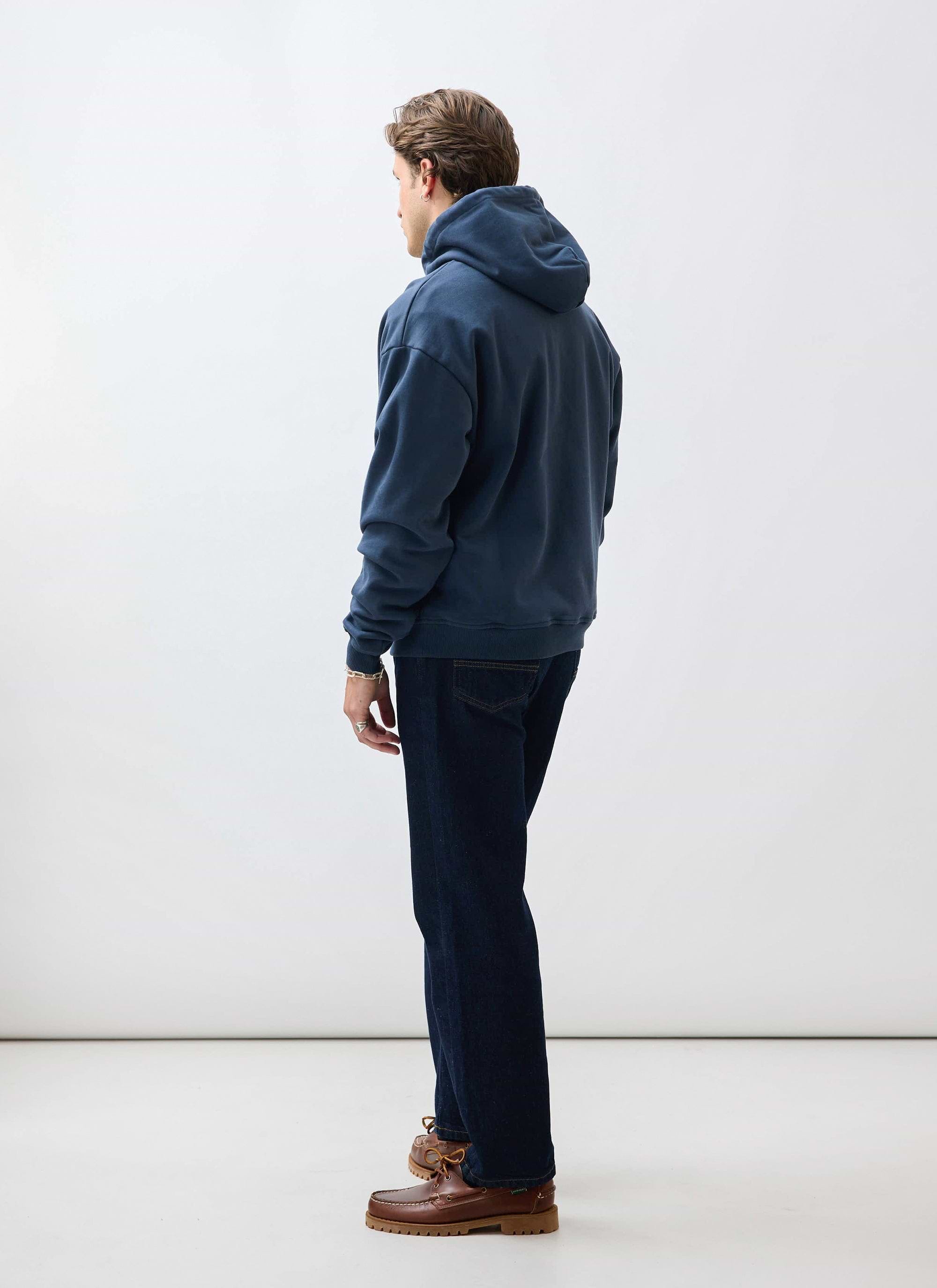 A model shot from behind wearing the Percival 'This Book Belongs To' hoodie in navy with dark wash jeans.