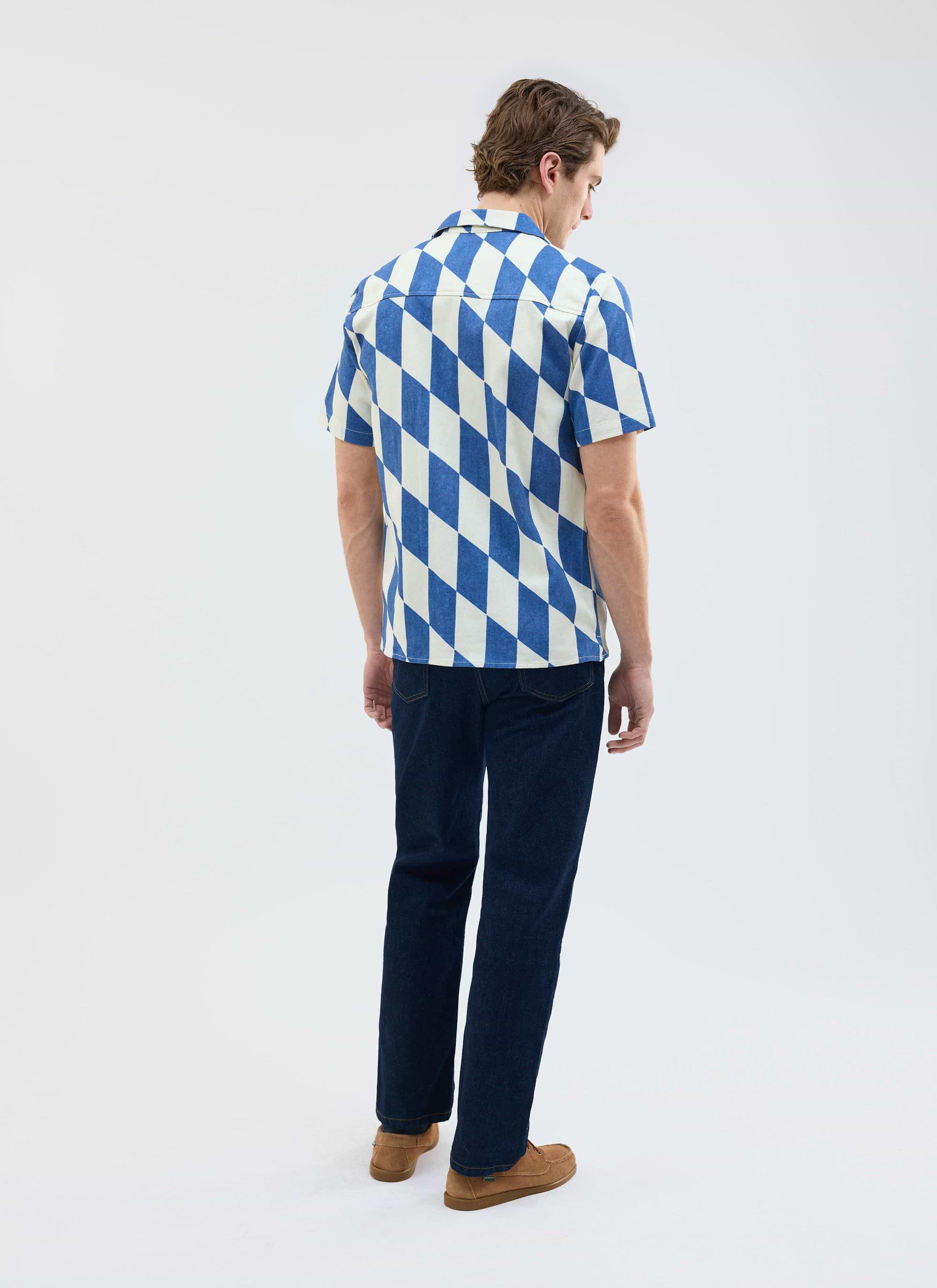 Back view of a model wearing the ecru and navy diamond print Market Cuban Shirt from Percival with dark jeans.