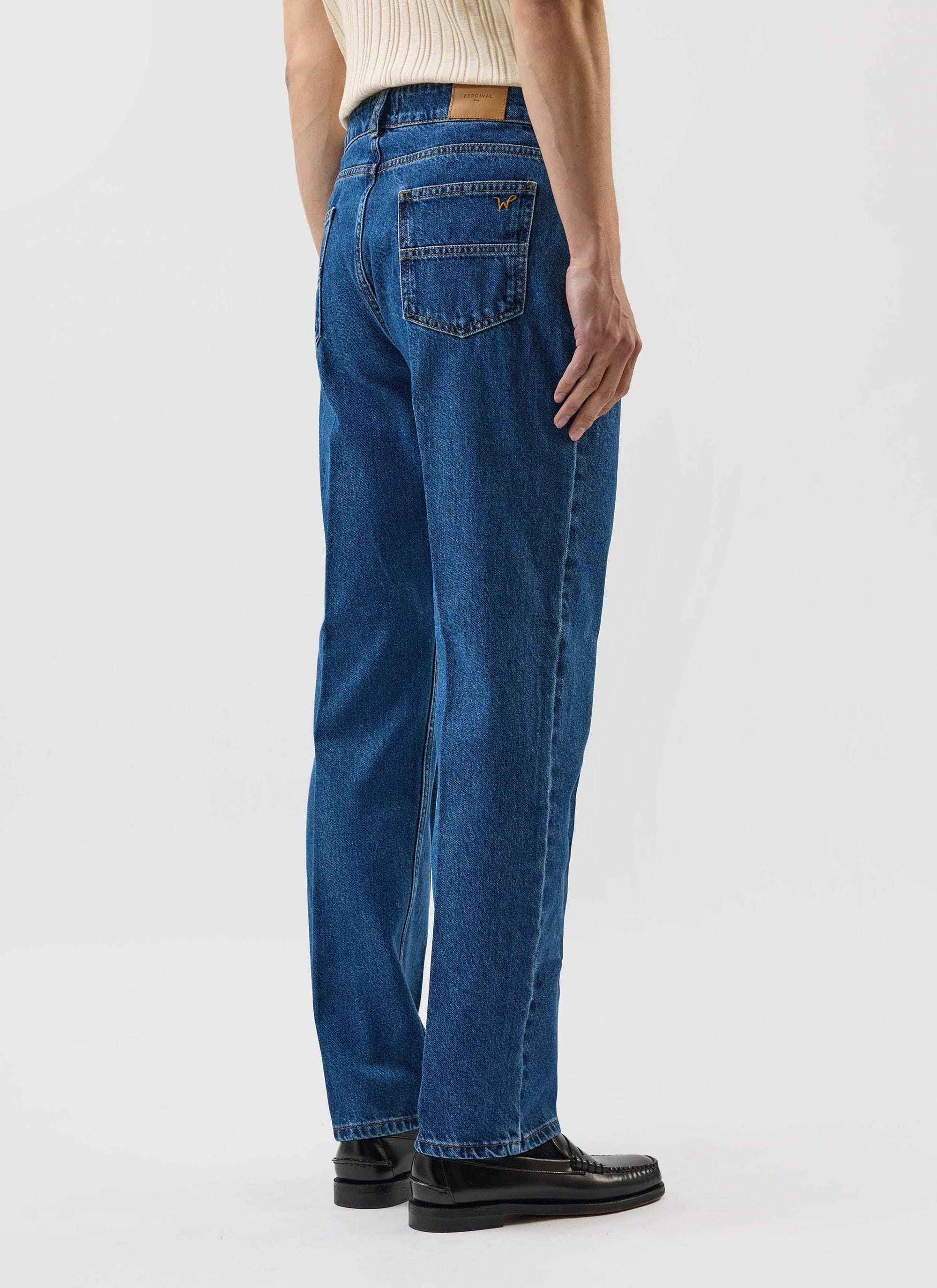 A back view of a model wearing the Percival x Warren Stay Press Denim Jeans in a mid-wash blue, showing the pocket detail.