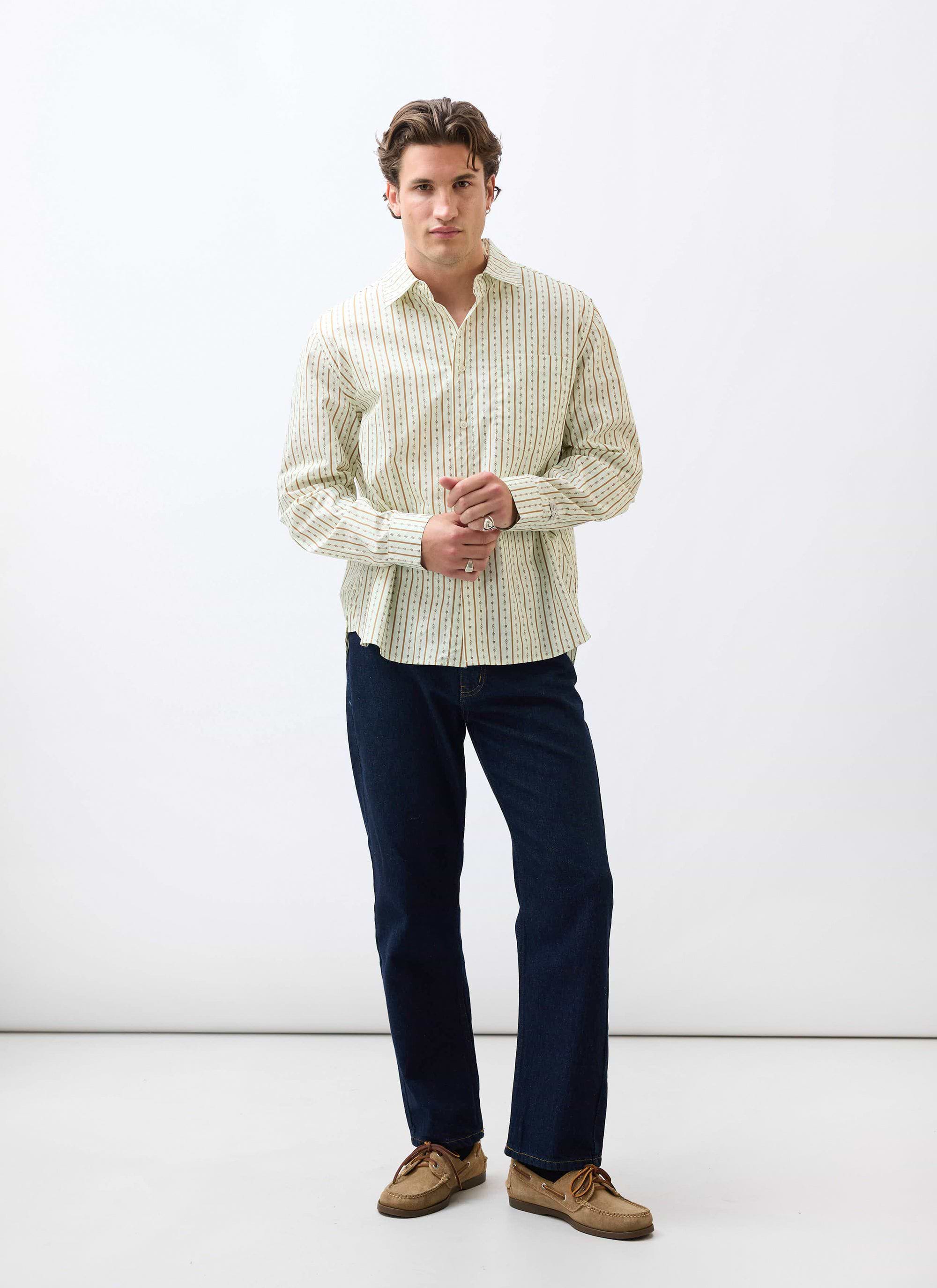A model stands against a white background wearing the Percival Binding Oversized Pearce Shirt in ecru with dark jeans.