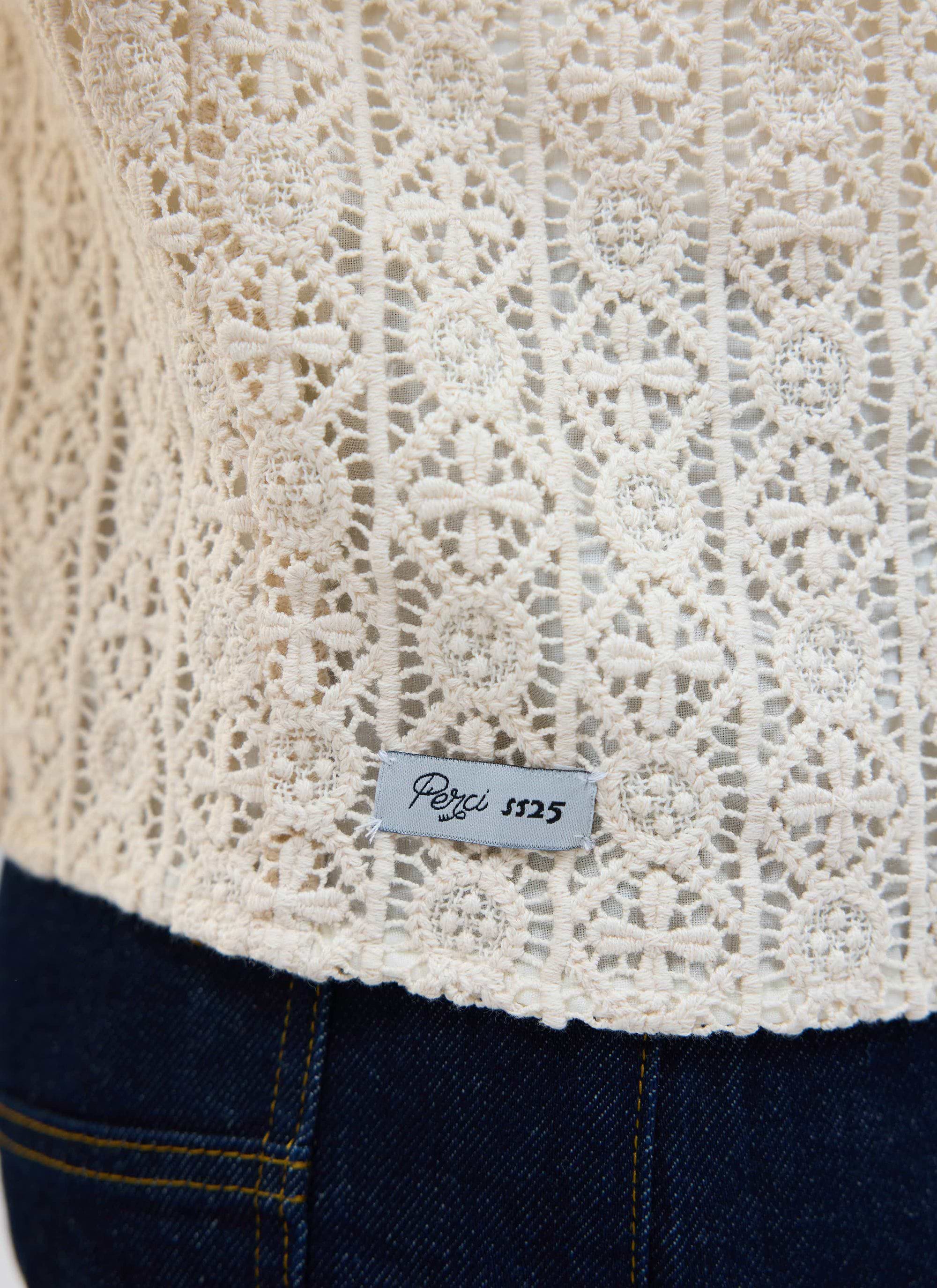 A close-up of the intricate crochet pattern and SS25 label on the ecru Elio Cuban Shirt by Percival.